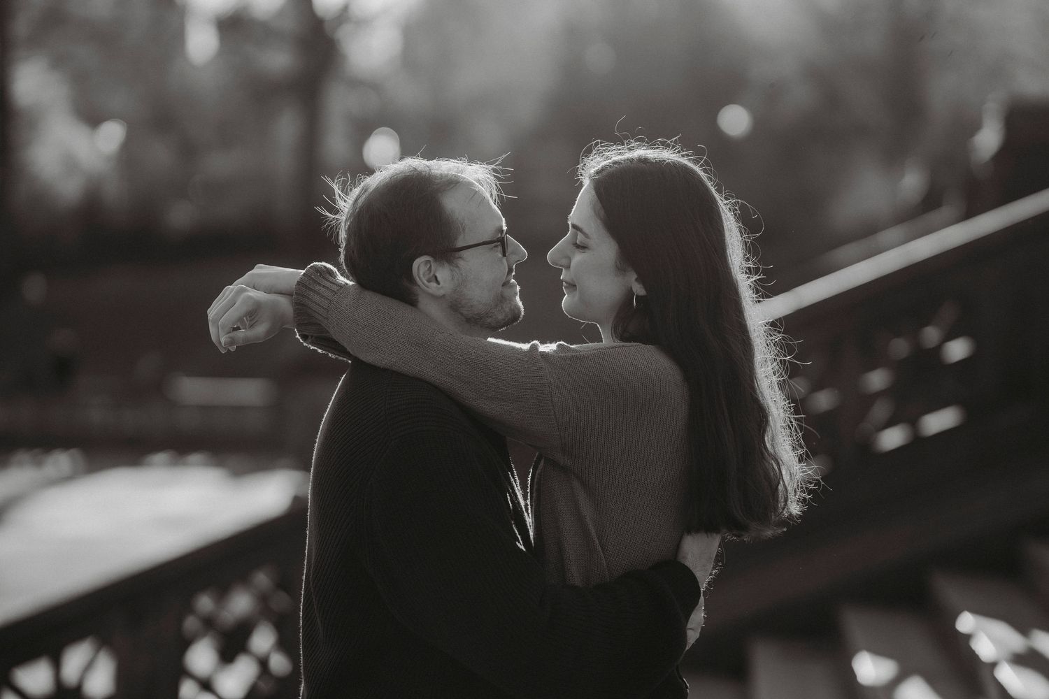 Black and white romantic photo of a couple embracing face-to-face on an outdoor bridge.