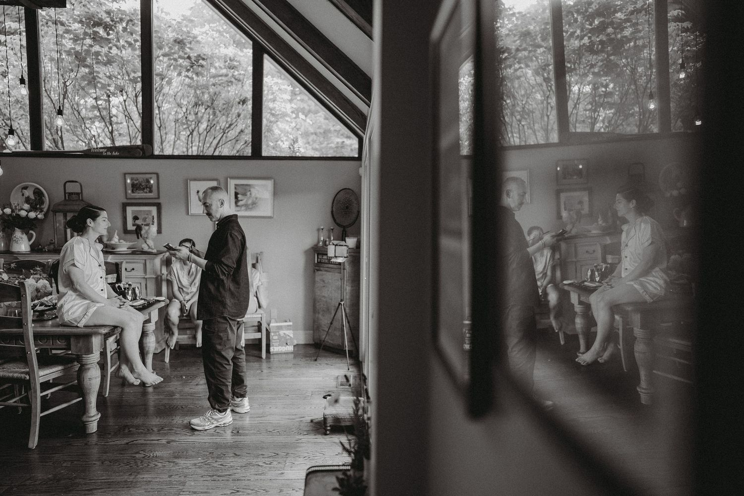 Black and white photo of people gathered in a sunlit studio with large windows and framed artwork.