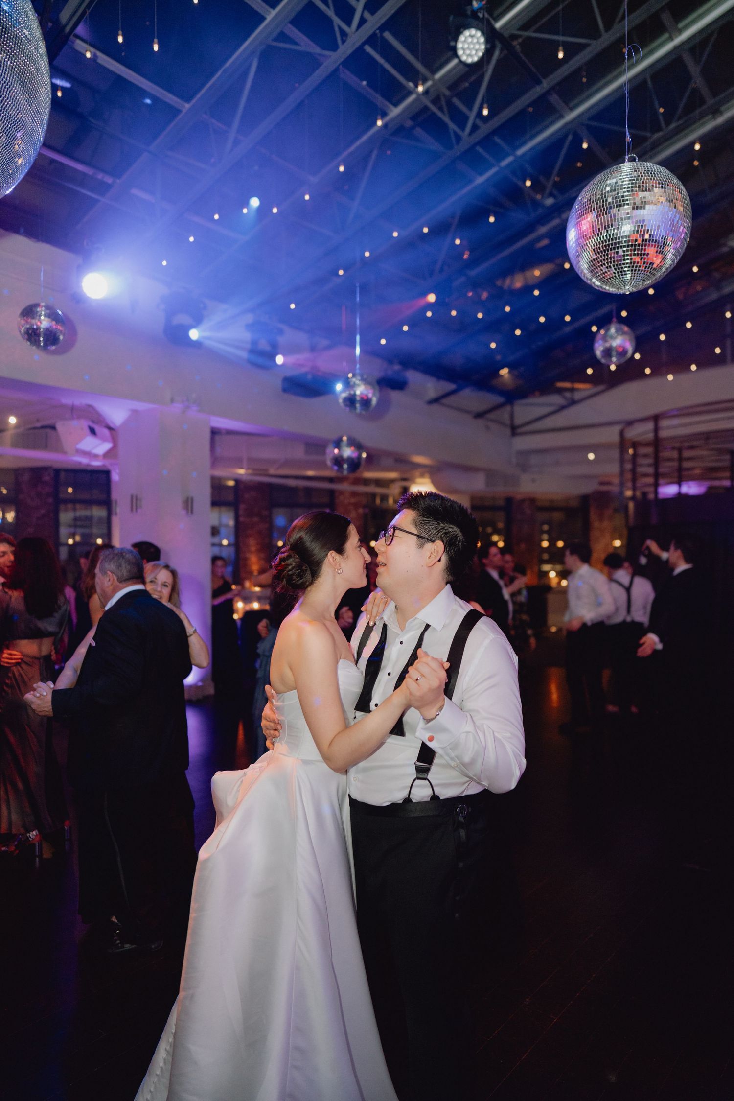 Bride and groom share an intimate slow dance under sparkling disco balls at their wedding reception.