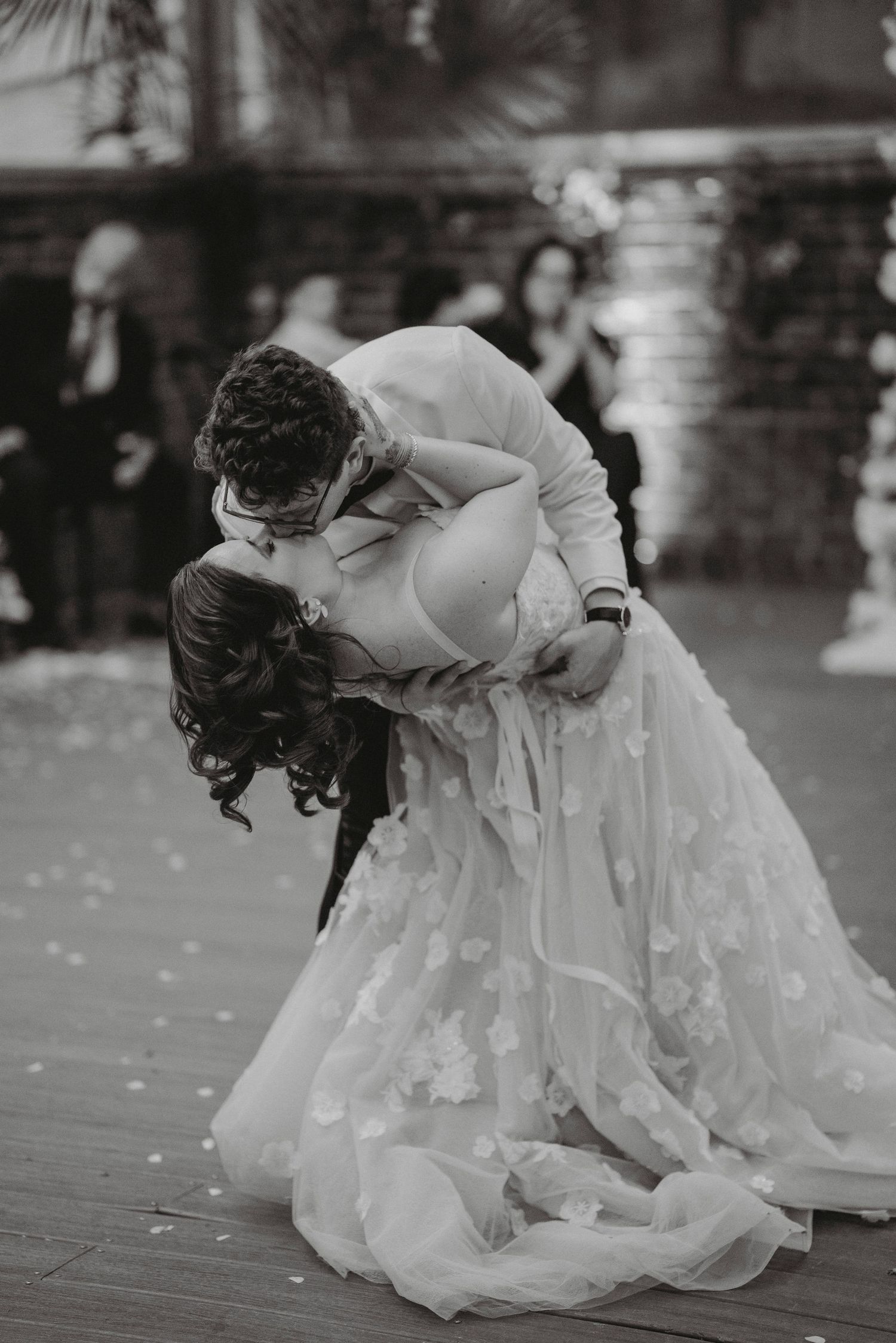 Black and white photo of groom dipping bride for a romantic kiss during their first dance outdoors.