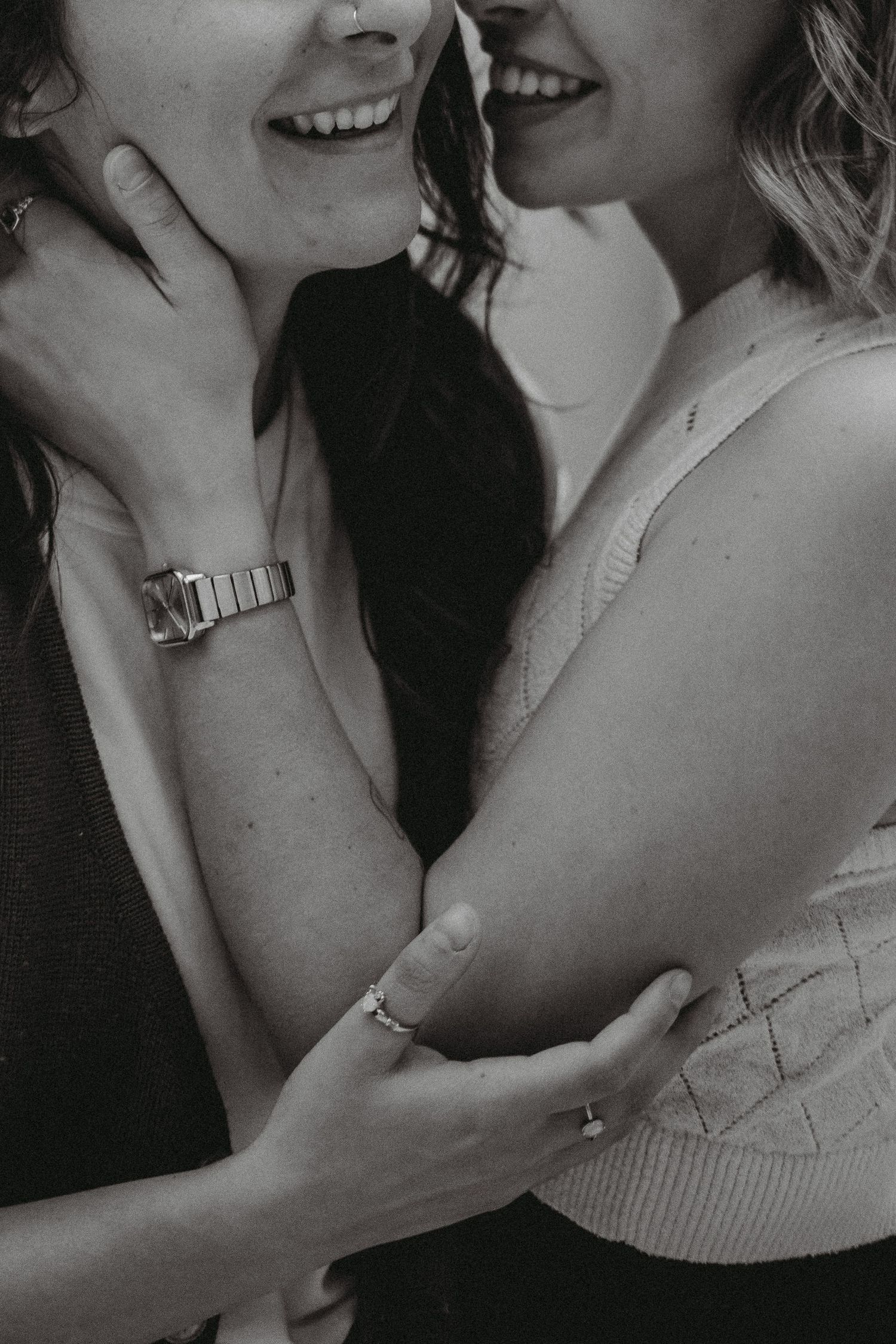 Close-up of two women embracing and laughing together, showing rings and a silver watch.