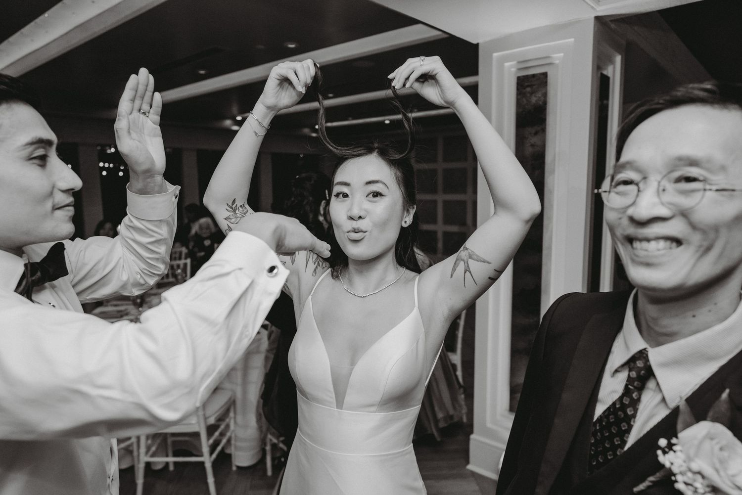 Bride dances joyfully with guests during a lively wedding reception celebration in black and white.