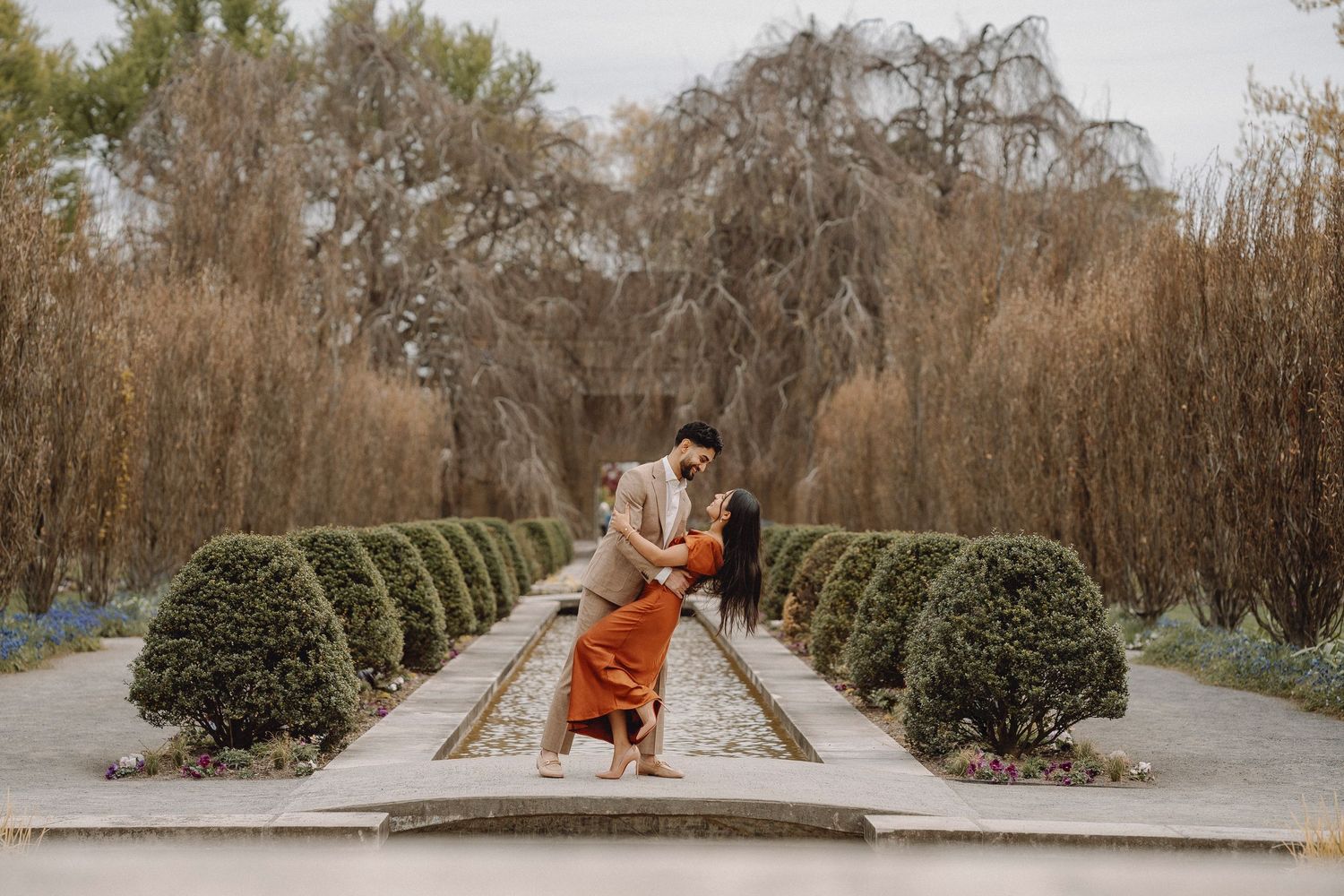 Couple sharing a romantic dip pose on a garden pathway flanked by manicured hedgerows.