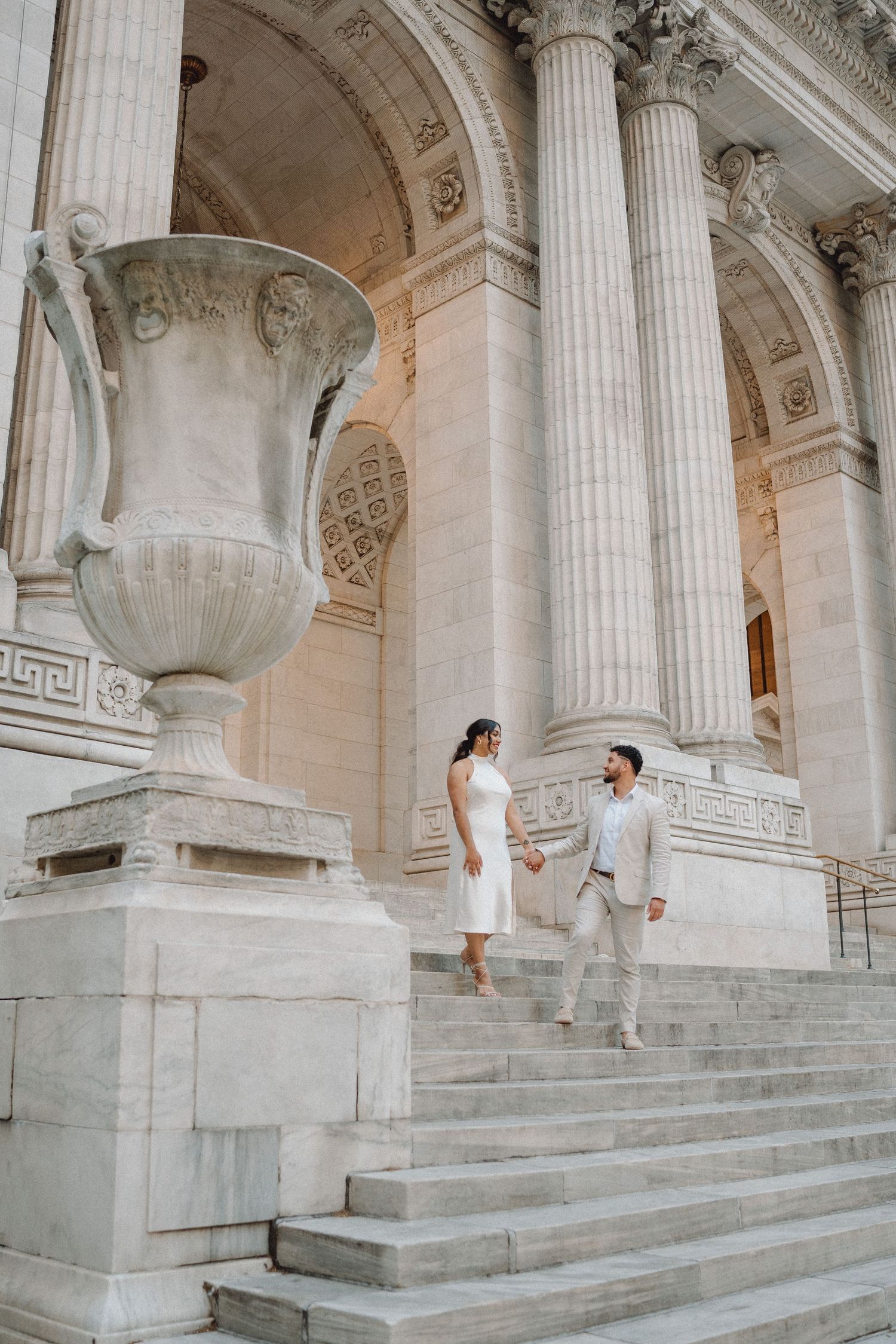 Elegant couple holding hands on the grand steps of the New York Public Library in wedding attire.