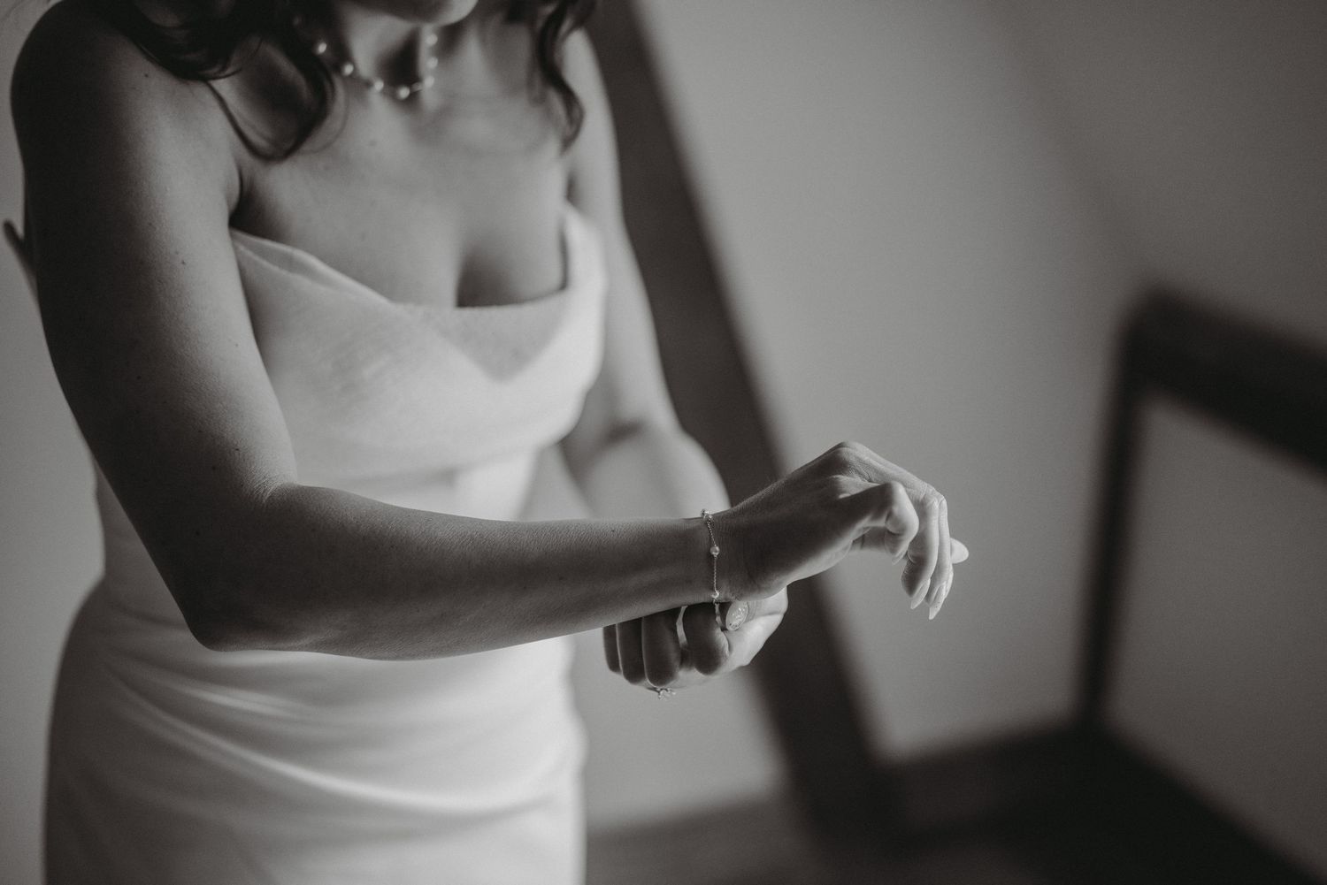 Black and white close-up of bride in strapless gown adjusting bracelet on her wrist.