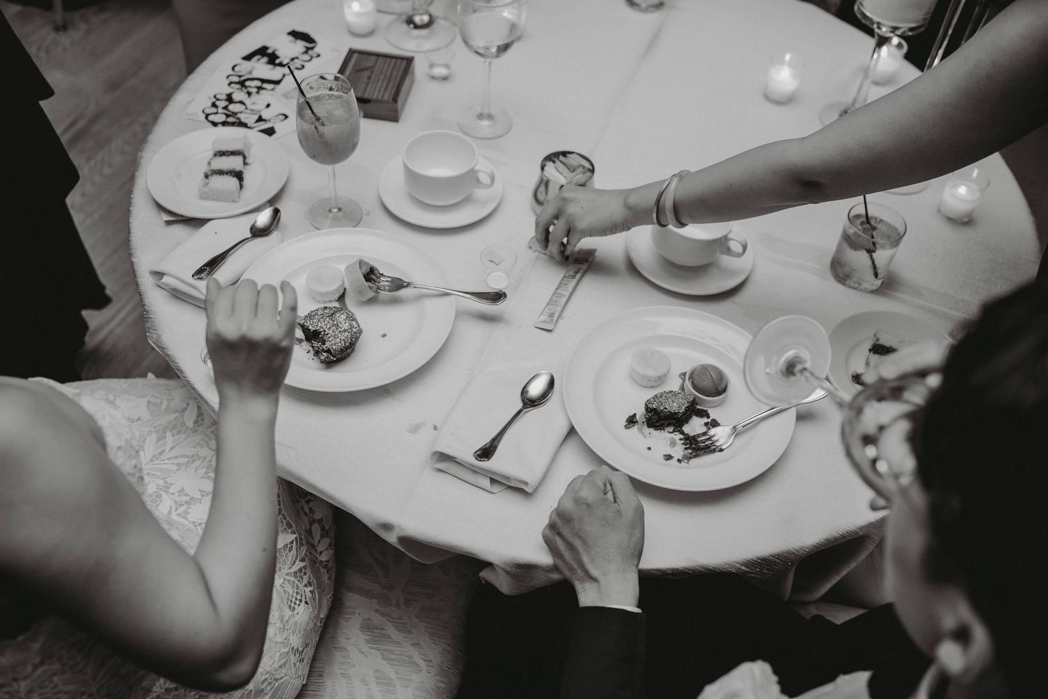 Overhead black and white shot of wedding guests enjoying dessert at candlelit reception table.