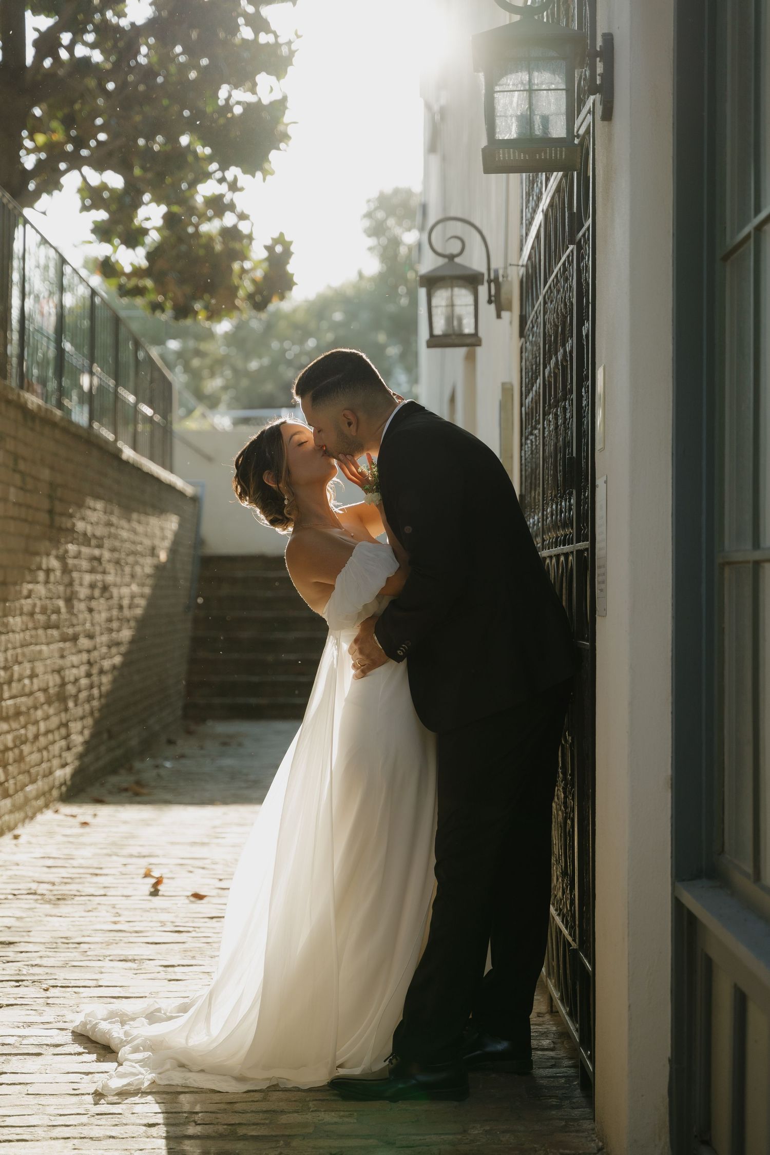 A bride and groom share a romantic kiss against a sunlit wall on their wedding day in Sacramento, CA