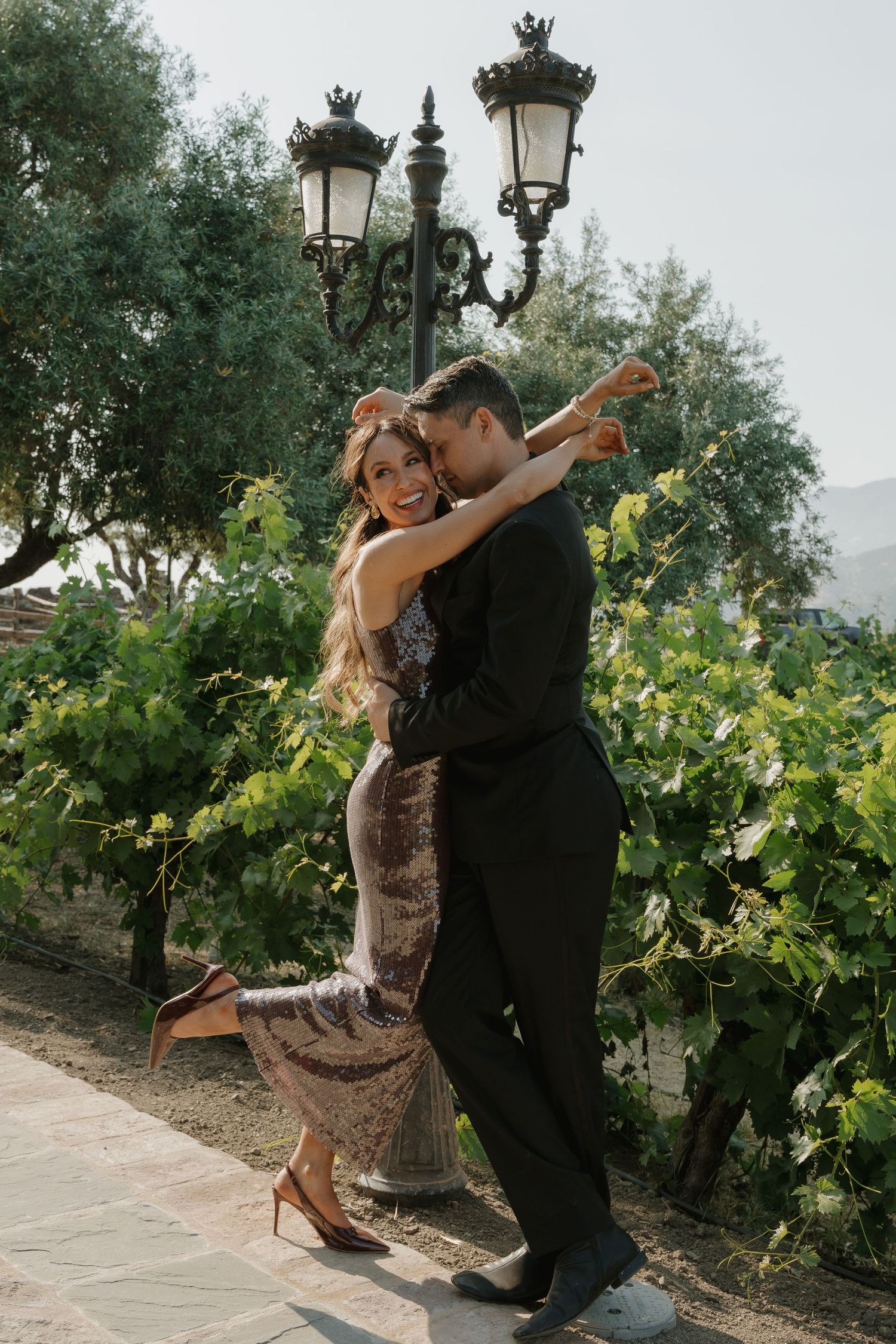 Couple dancing romantically near ornate street lamp with green vineyard and mountains in background in Napa, CA.