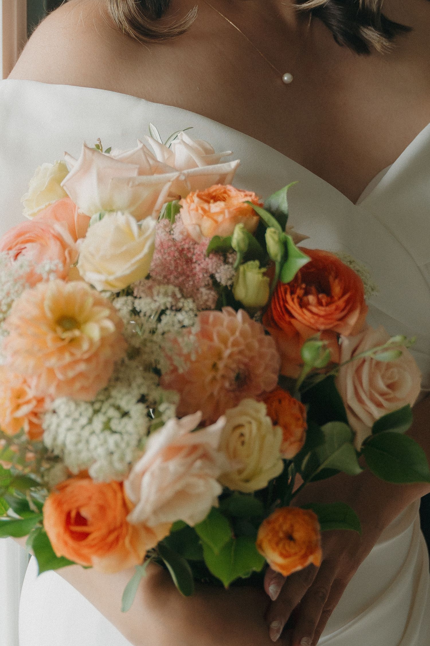 Bride holding a lush peach and cream wedding bouquet with roses, dahlias, and greenery in a white gown.