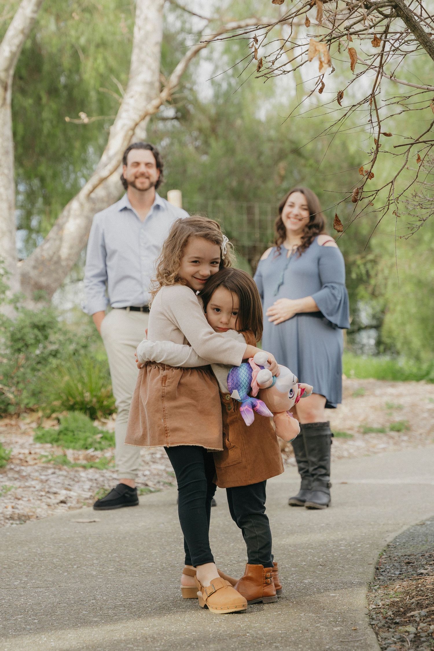 Two young girls hugging on a path while their parents stand behind them in a park setting at Walnut Creek, CA.