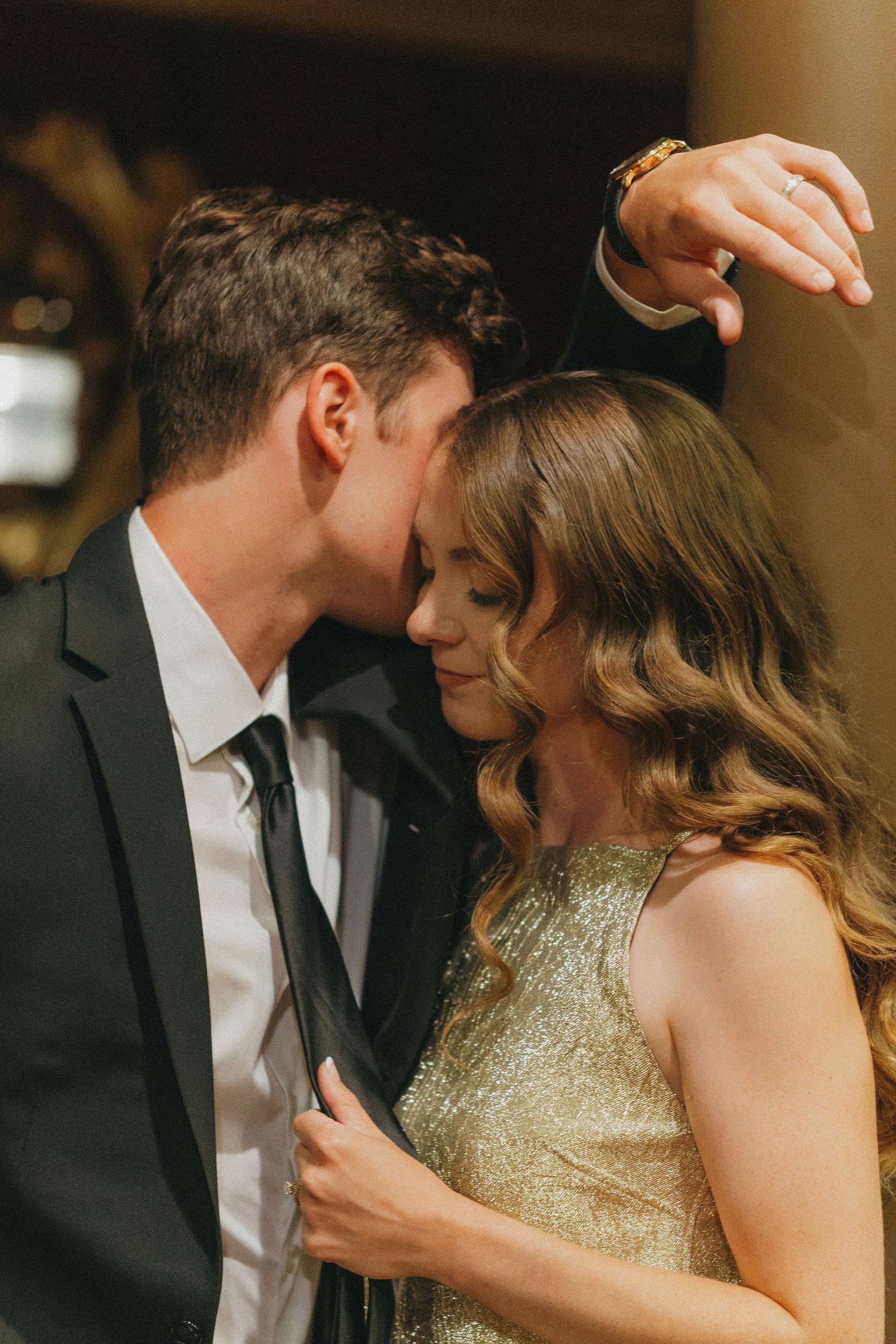 Romantic couple in elegant attire sharing an intimate moment, man in suit kissing woman in gold sequin dress.