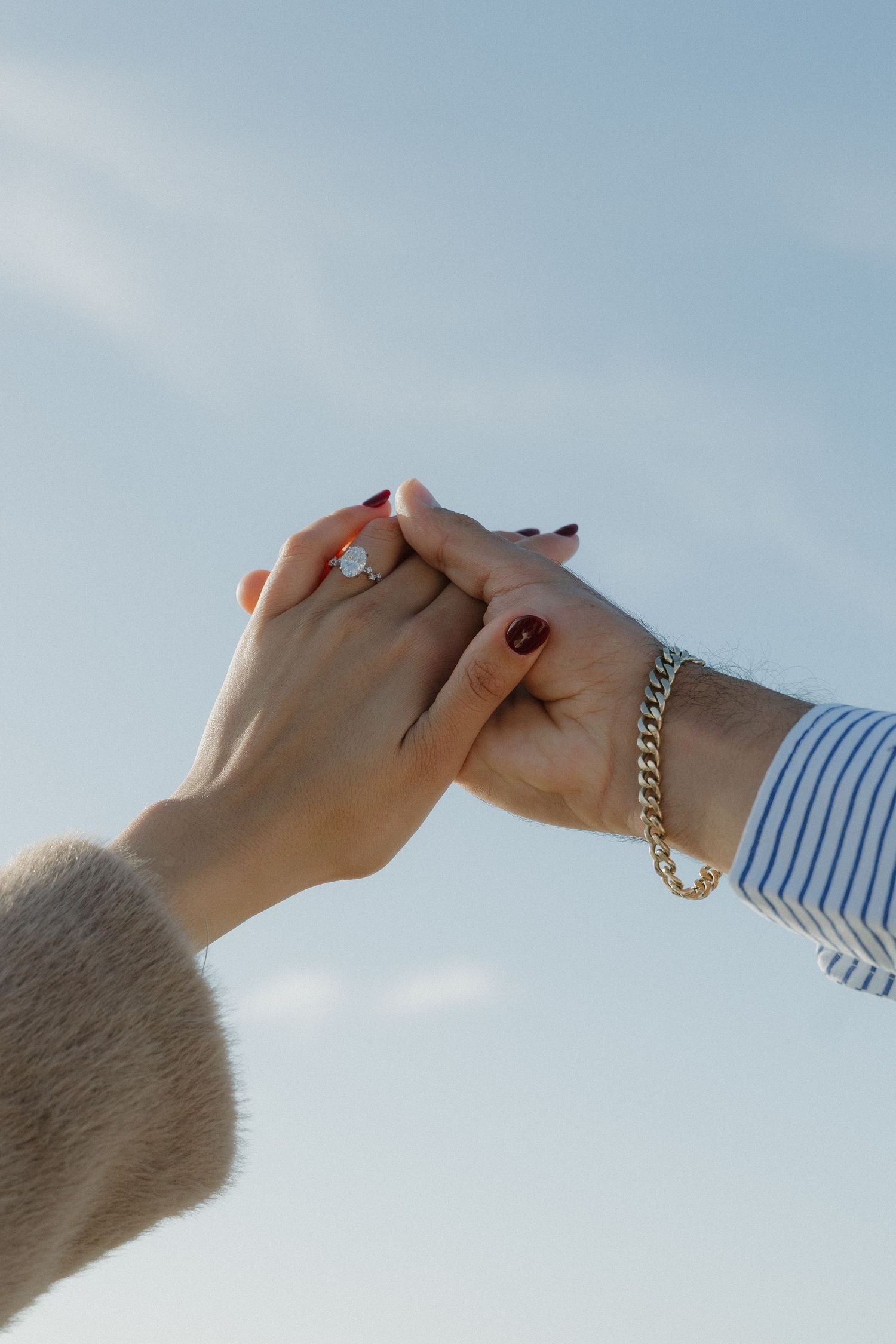 Close-up of two hands held together against a blue sky, woman wearing a diamond engagement ring at Half Moon Bay.