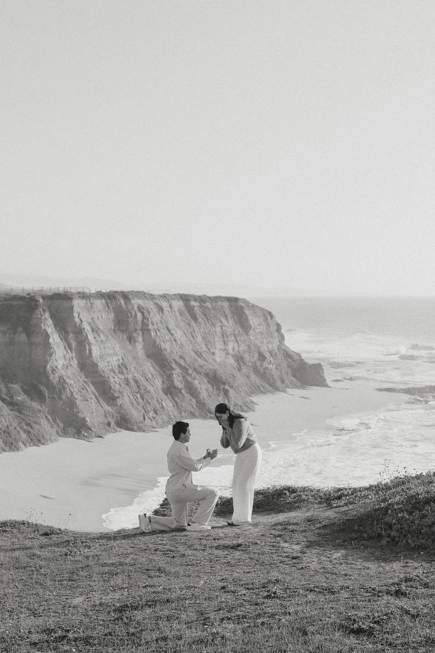 Man proposes to woman overlooking the beach cliffside in Half Moon Bay, CA.