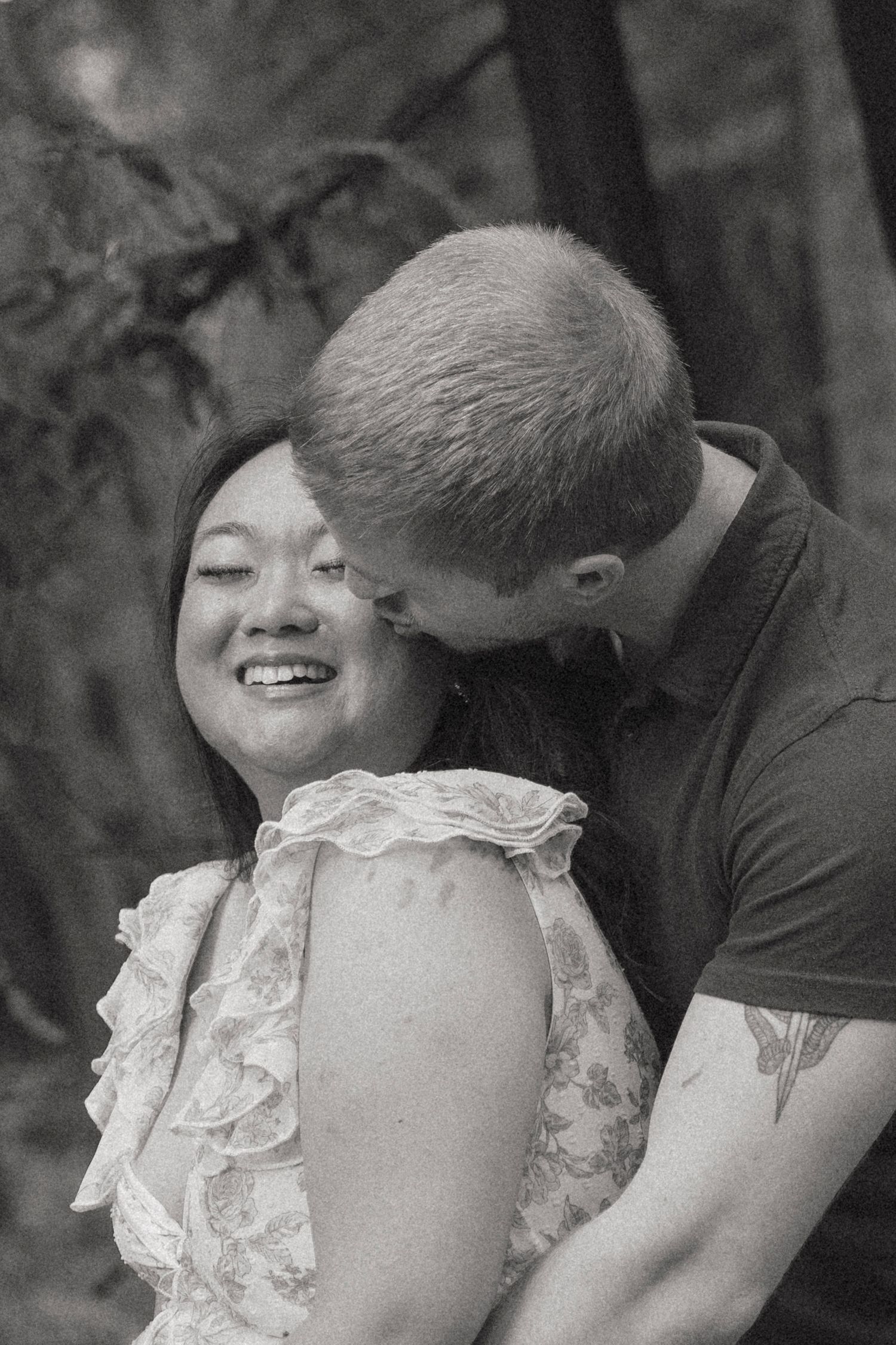 Black and white photo of a smiling woman being kissed on the cheek by her partner outdoors in Santa Cruz, CA.