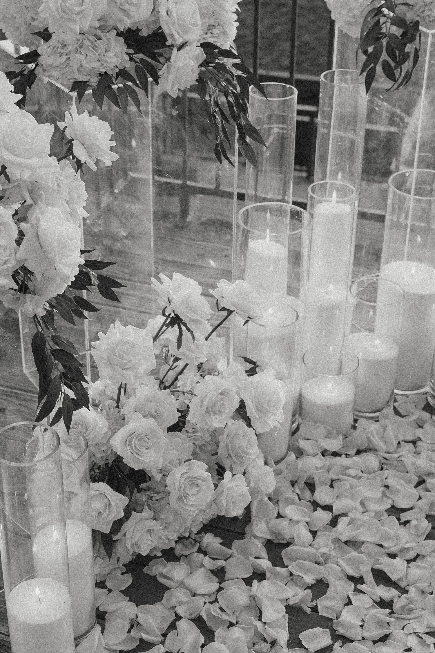 Elegant black and white wedding floral arrangement with white roses, candles, and scattered rose petals at Monterey, CA.