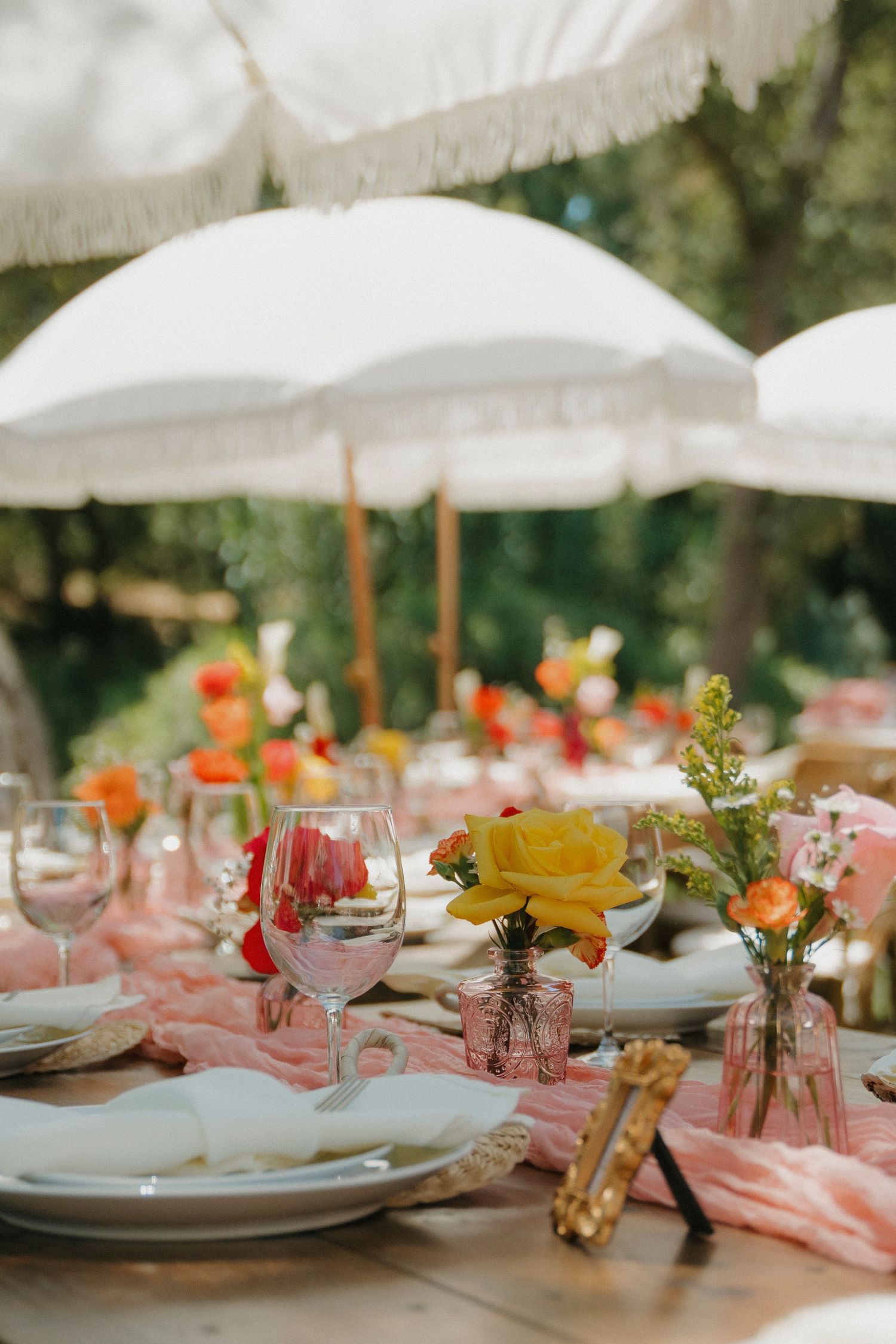 Elegant outdoor wedding reception table with colorful floral arrangements under white fringed umbrellas.