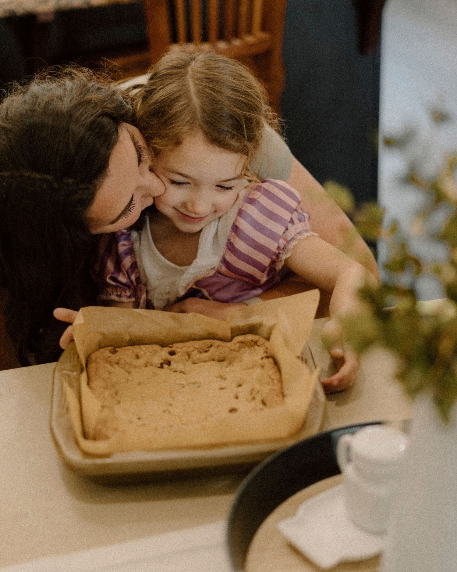 Mother and young daughter smiling over homemade cookie dough in a baking pan at kitchen table at Pleasanton, CA.