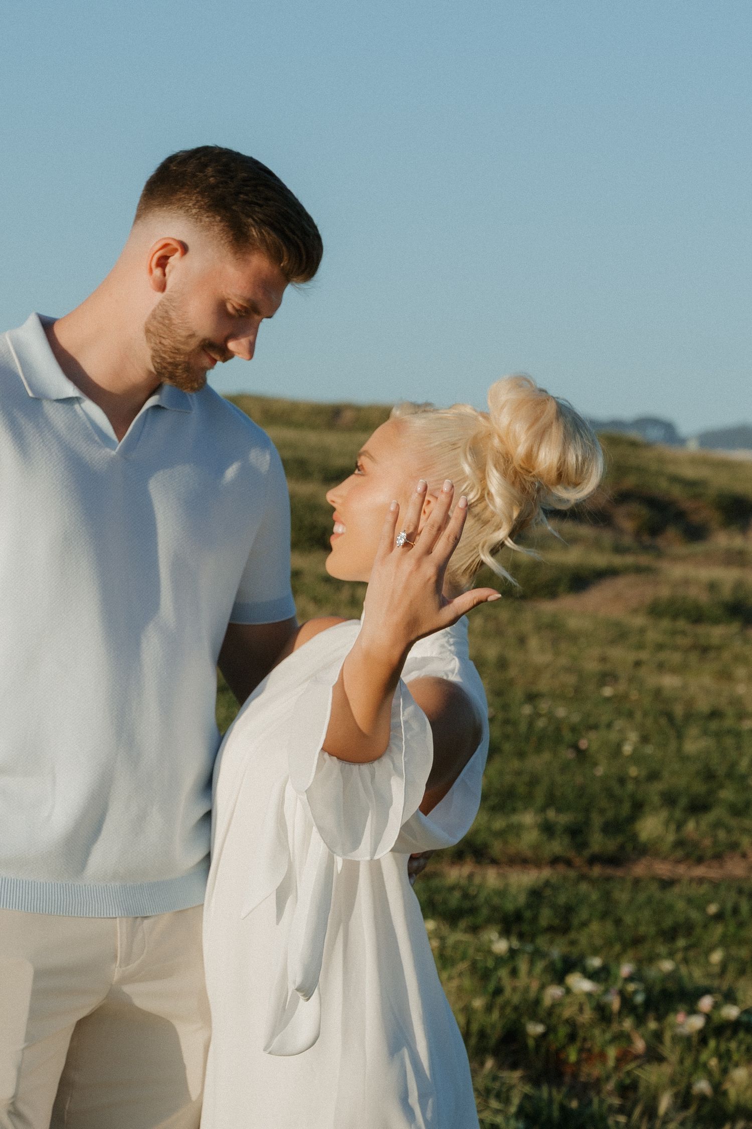 Romantic couple in white outfits sharing an intimate moment in a sunlit green field at San Francisco, CA.