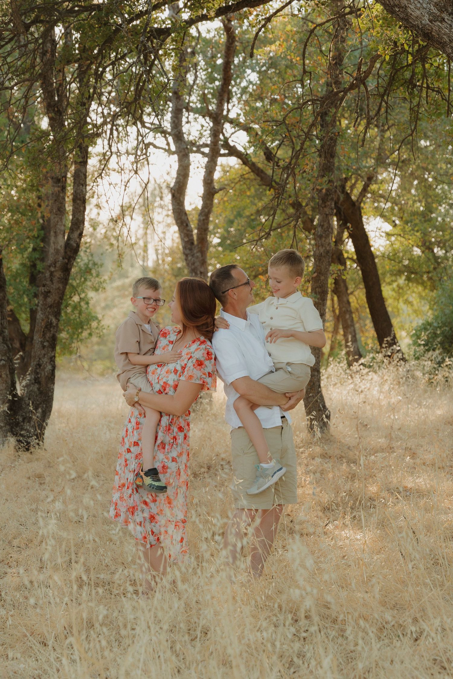 Happy family with two young boys in a golden sunlit forest clearing.