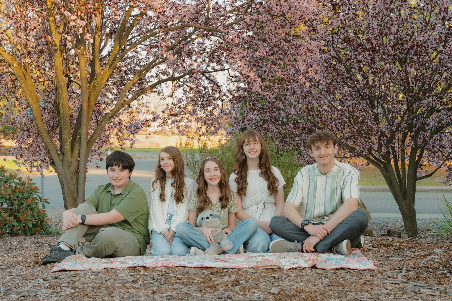 Five siblings sitting together on a blanket under blooming cherry blossom trees in autumn at El Dorado Hills, CA.