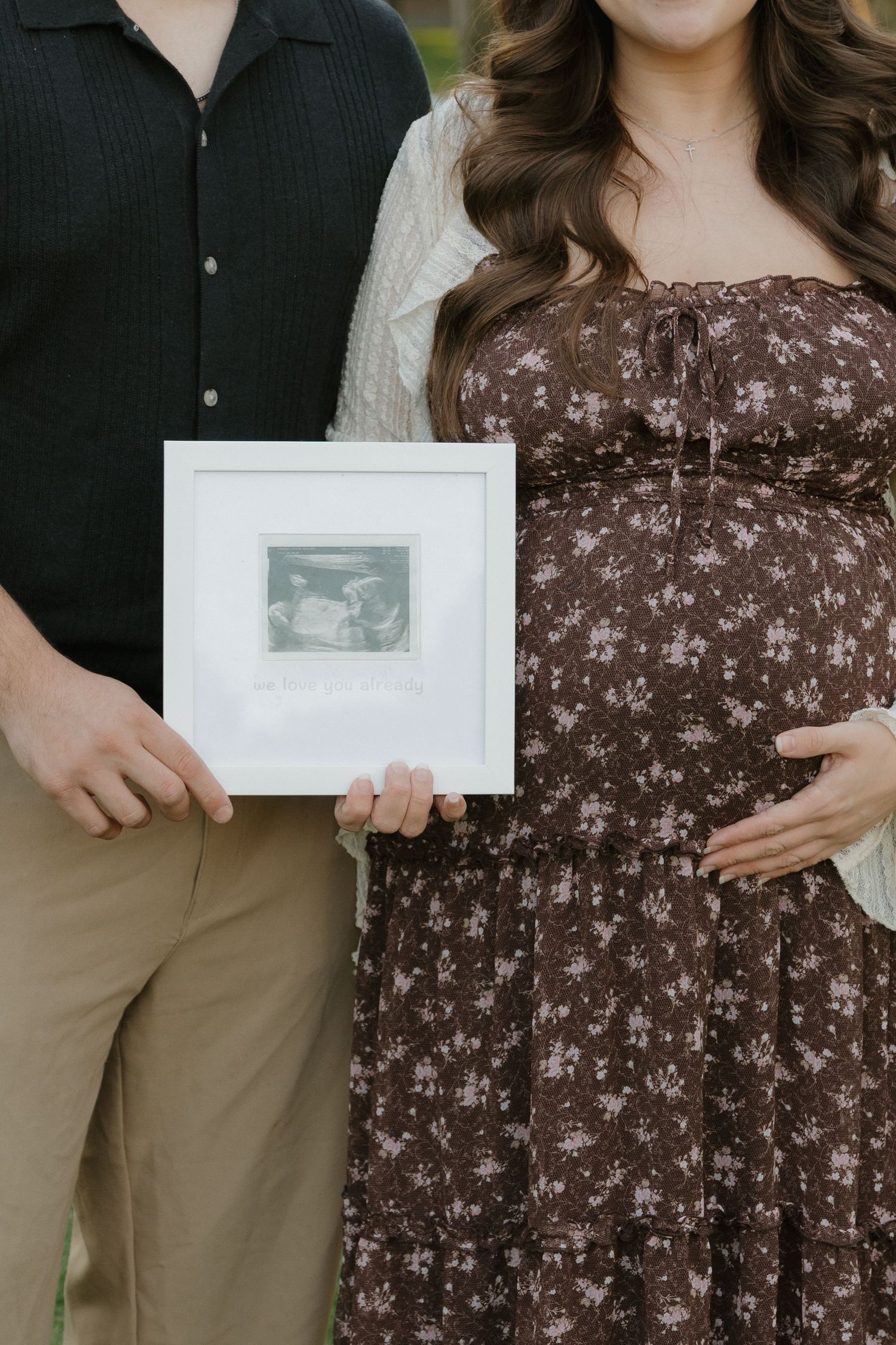 Pregnant couple holding framed ultrasound photo outdoors, woman in brown floral maternity dress in Redwood City, CA.