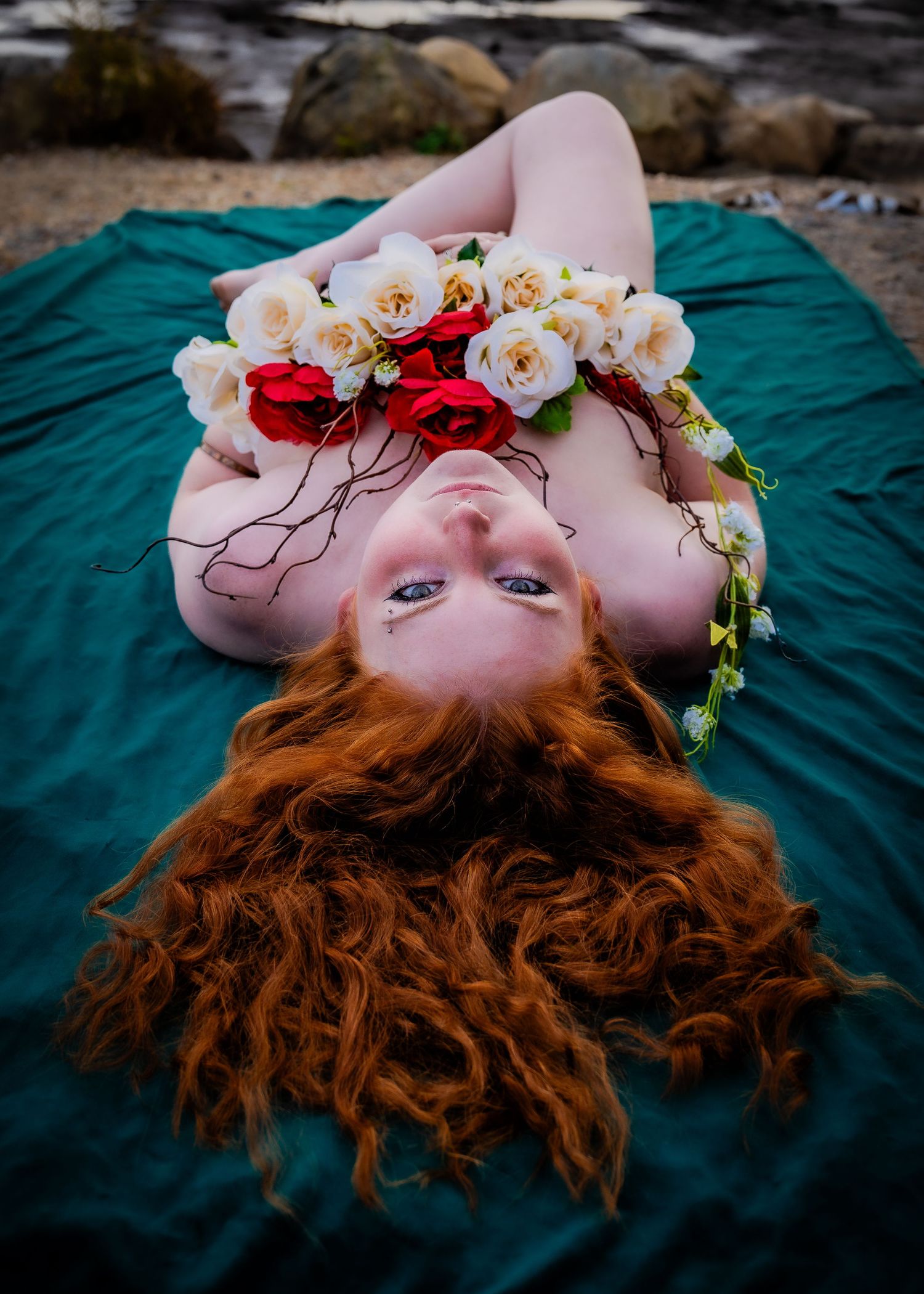 A series of artistic photos showing a person with long red hair lying on teal fabric with white roses in their hair.