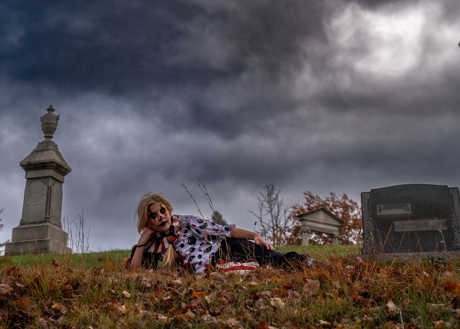 Moody cemetery scene with autumn leaves and stormy sky.