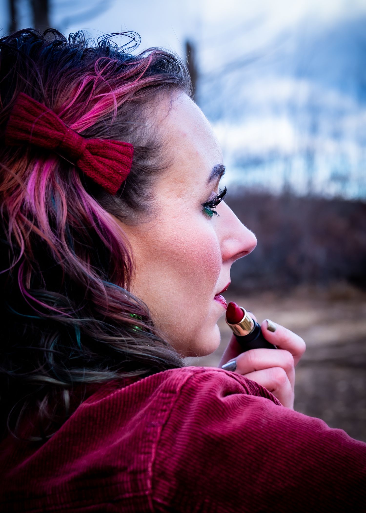 A person with vibrant pink hair wearing a burgundy sweater gazes thoughtfully into the distance at sunset.