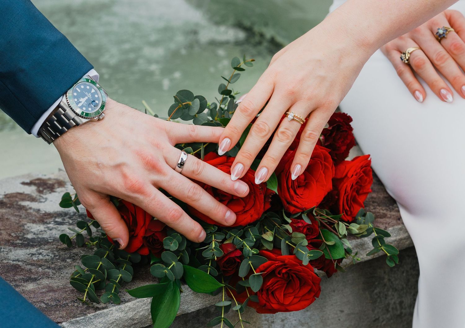 Close-up of bride and groom hands adorned with wedding rings resting on red roses at the cotton gin in Hiram Georgia.