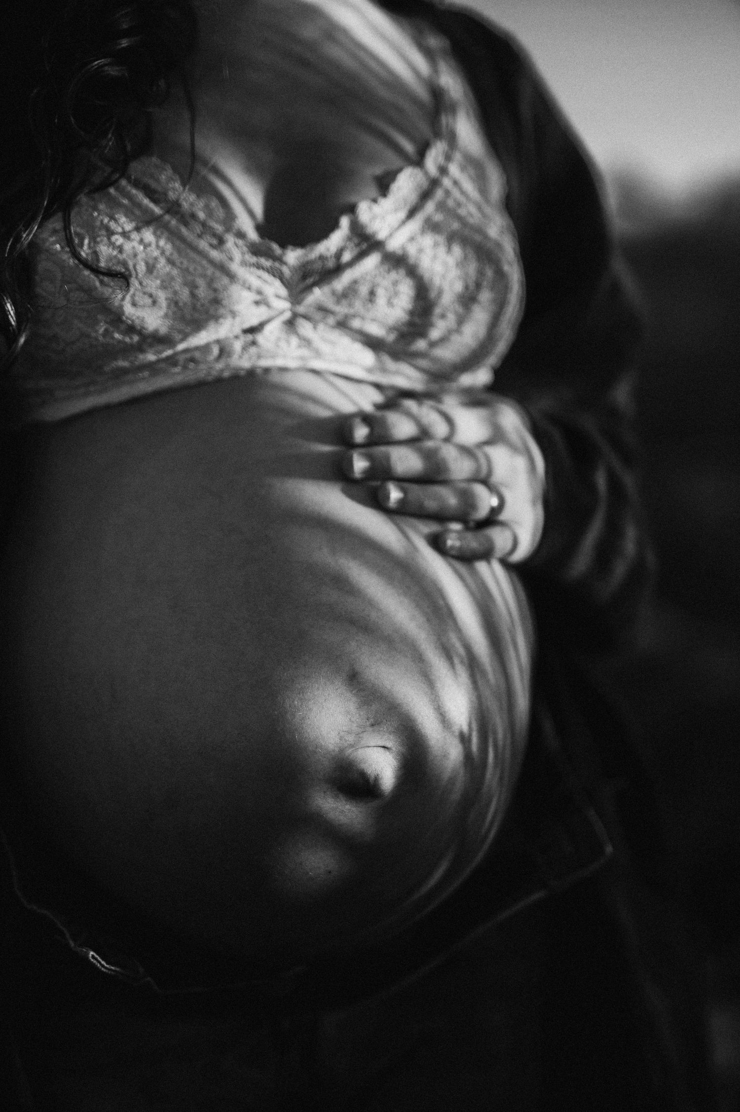 Svartvit gravidfotografering i Skåne med en gravid kvinna som håller sin gravidmage i mjukt ljus.