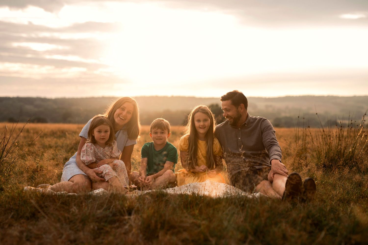 Familjefotografering i Skåne med familj på fem i gyllene fält vid solnedgång.