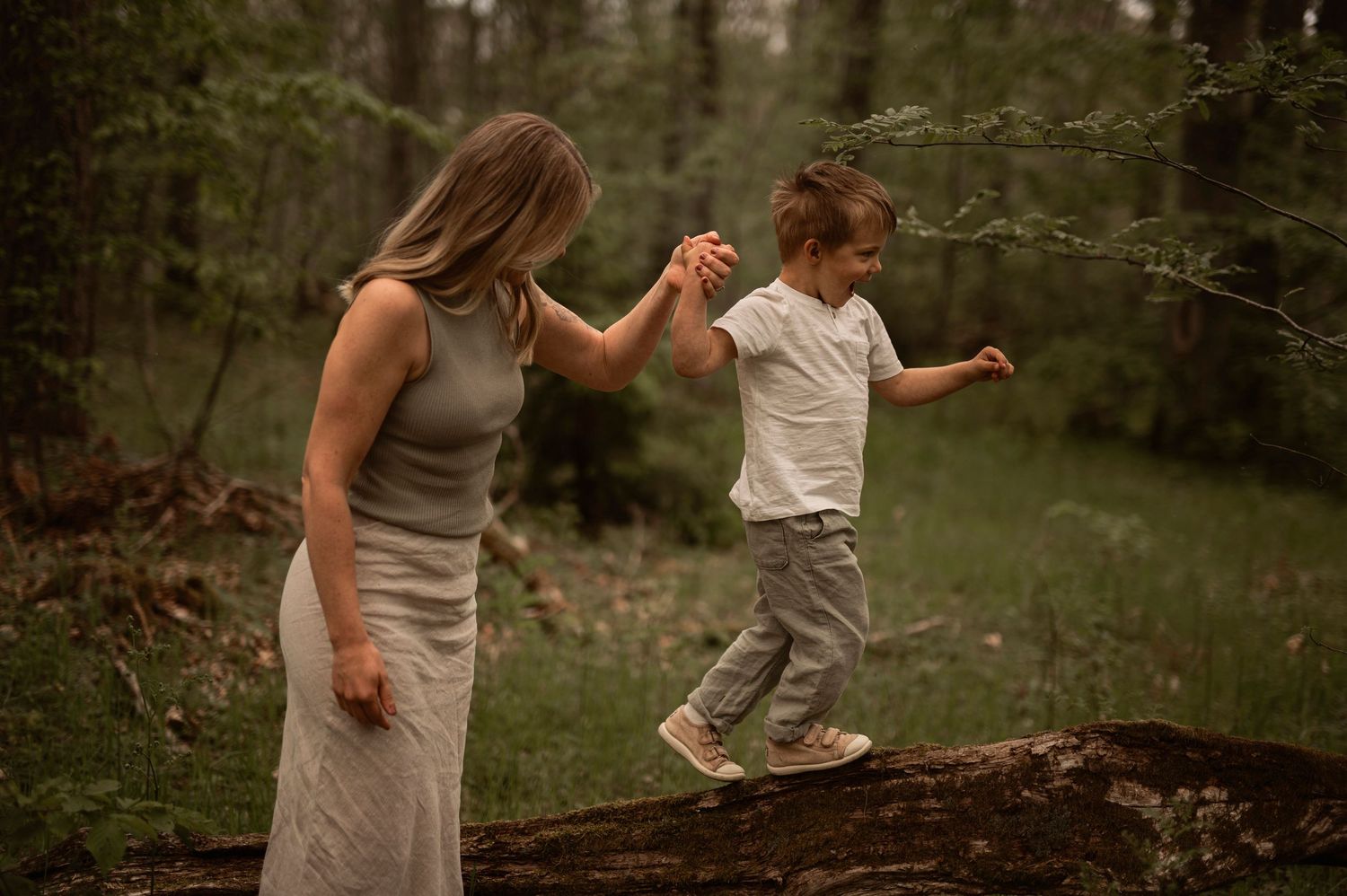 Familjefotografering i Skåne med mamma och son i lekfull balans på stock i skogsmiljö.