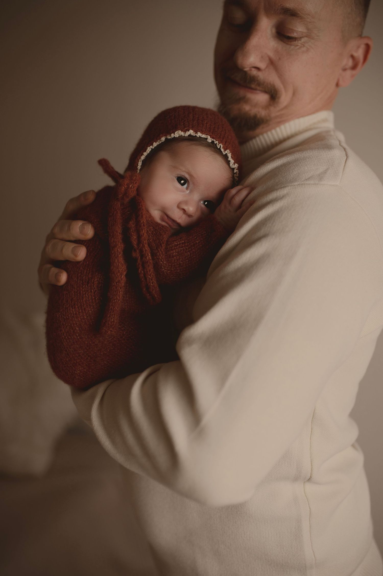 Parent in cream sweater holding baby wearing burgundy knit outfit and headband.