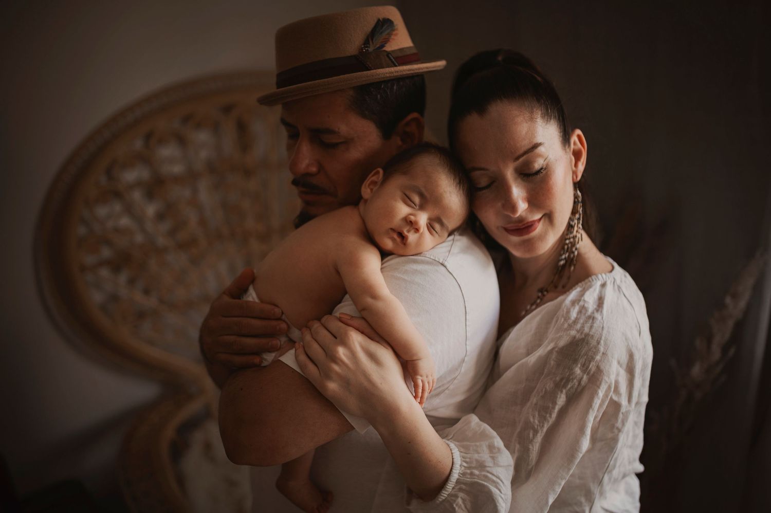 Tender family moment with sleeping infant held between two caregivers in warm lighting.