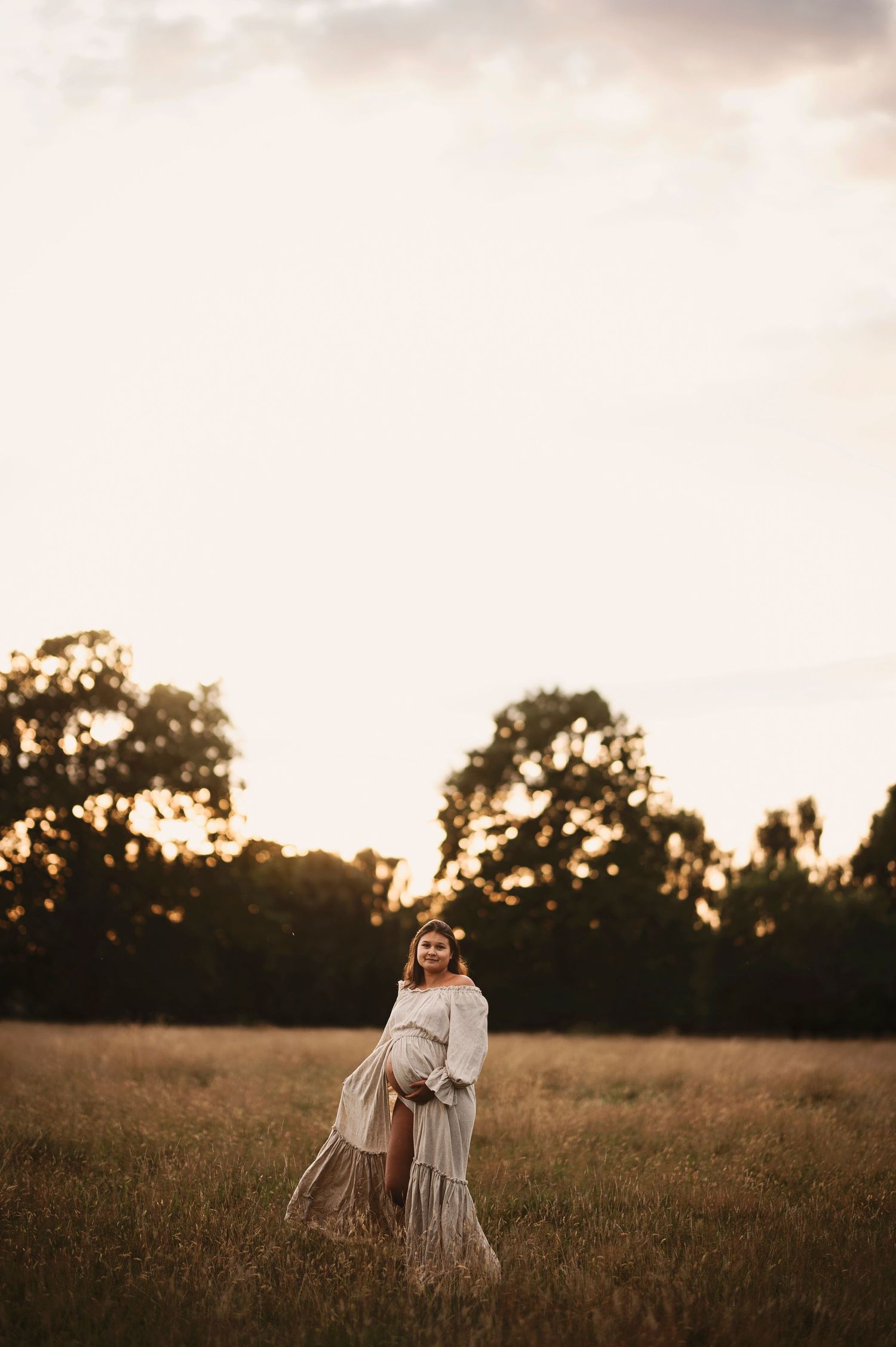 A flowy white dress silhouetted against a sunset field with trees in the background.