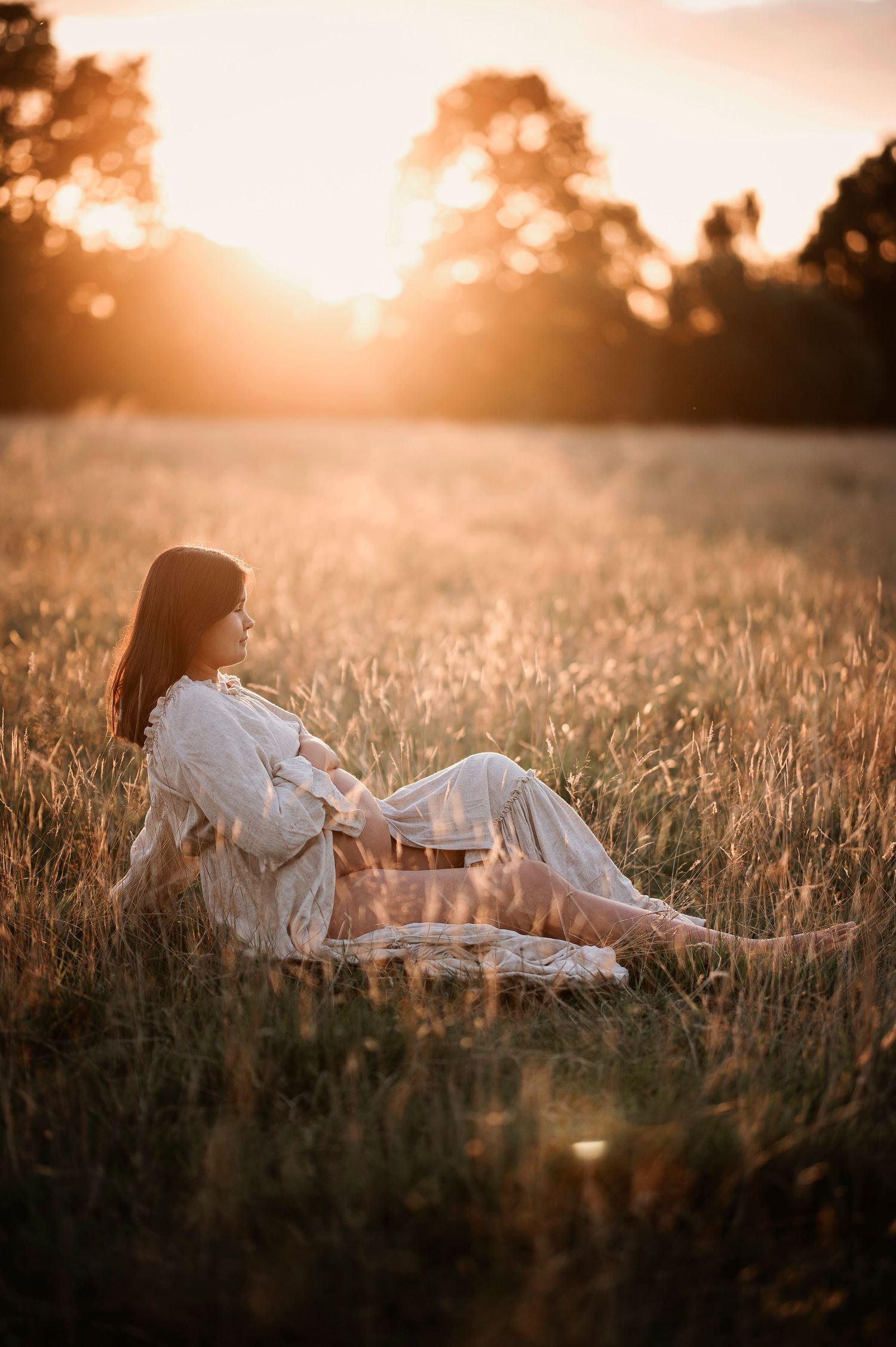 Woman in white dress relaxing on blanket in sun-drenched meadow during golden hour.