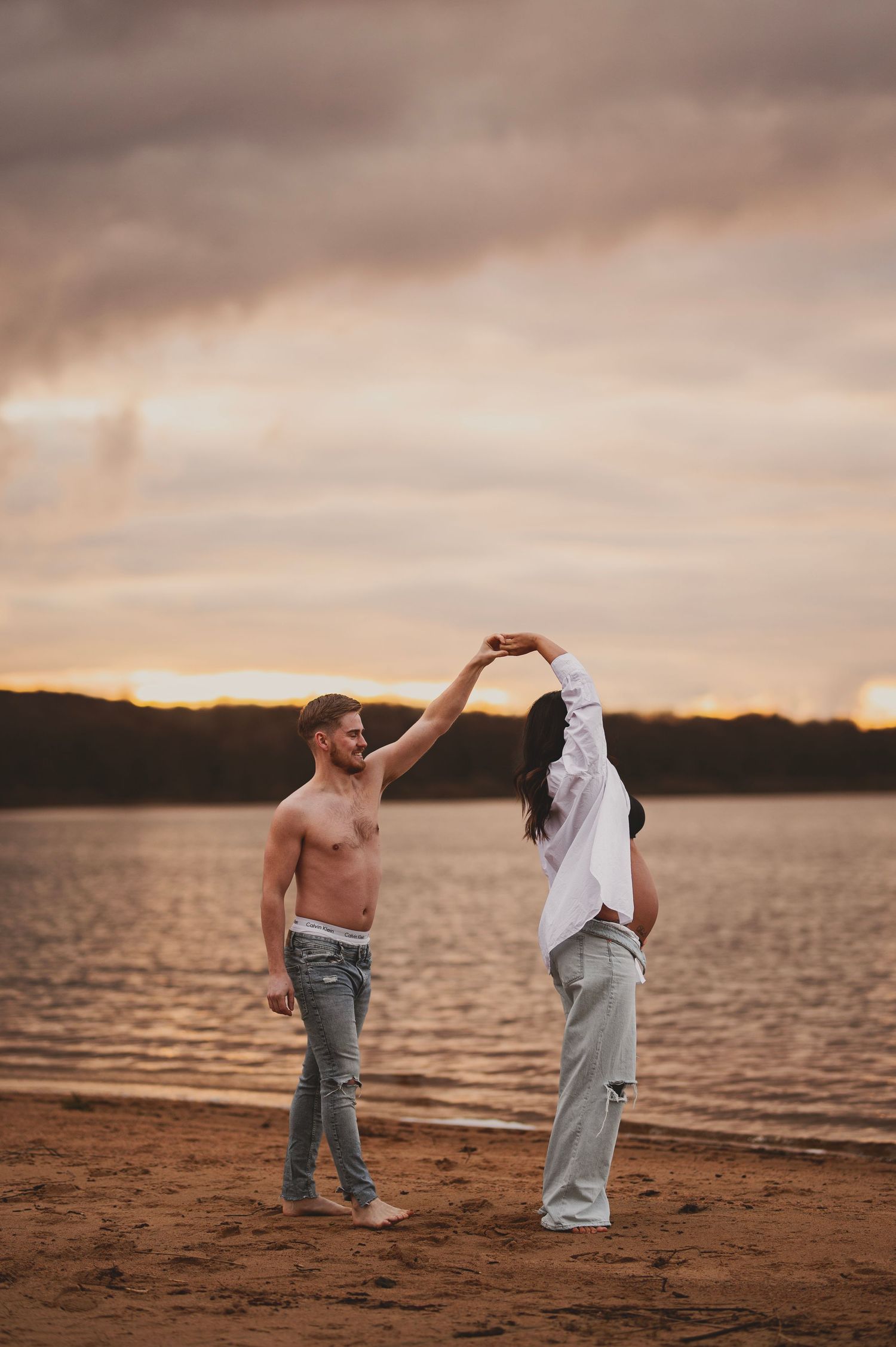 Couple dancing on beach at sunset with golden light reflecting on water.