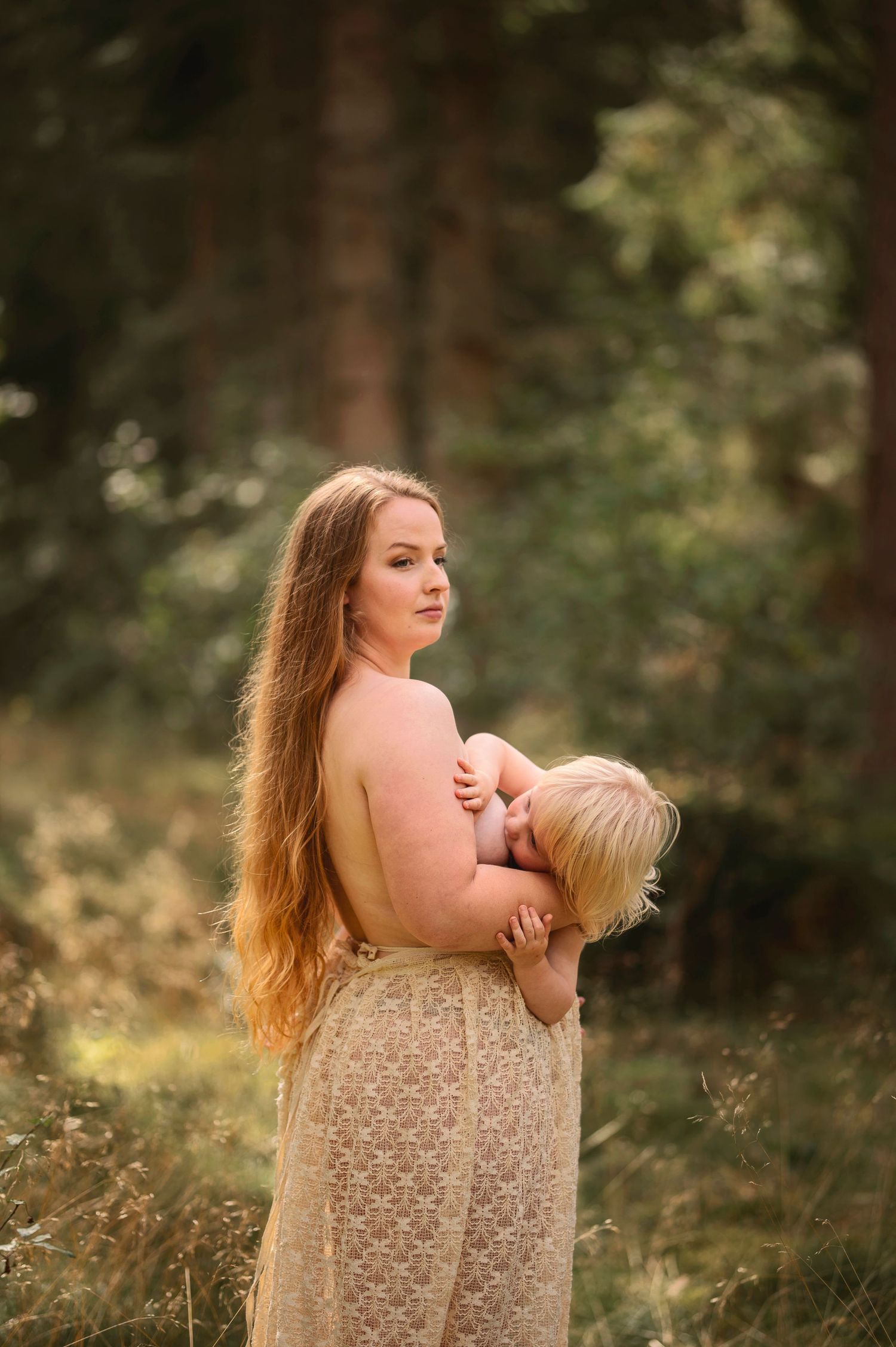 Moderskapsfotografering i Skåne med förälder som håller ett litet barn i spetsklänning i drömlik skogsmiljö.