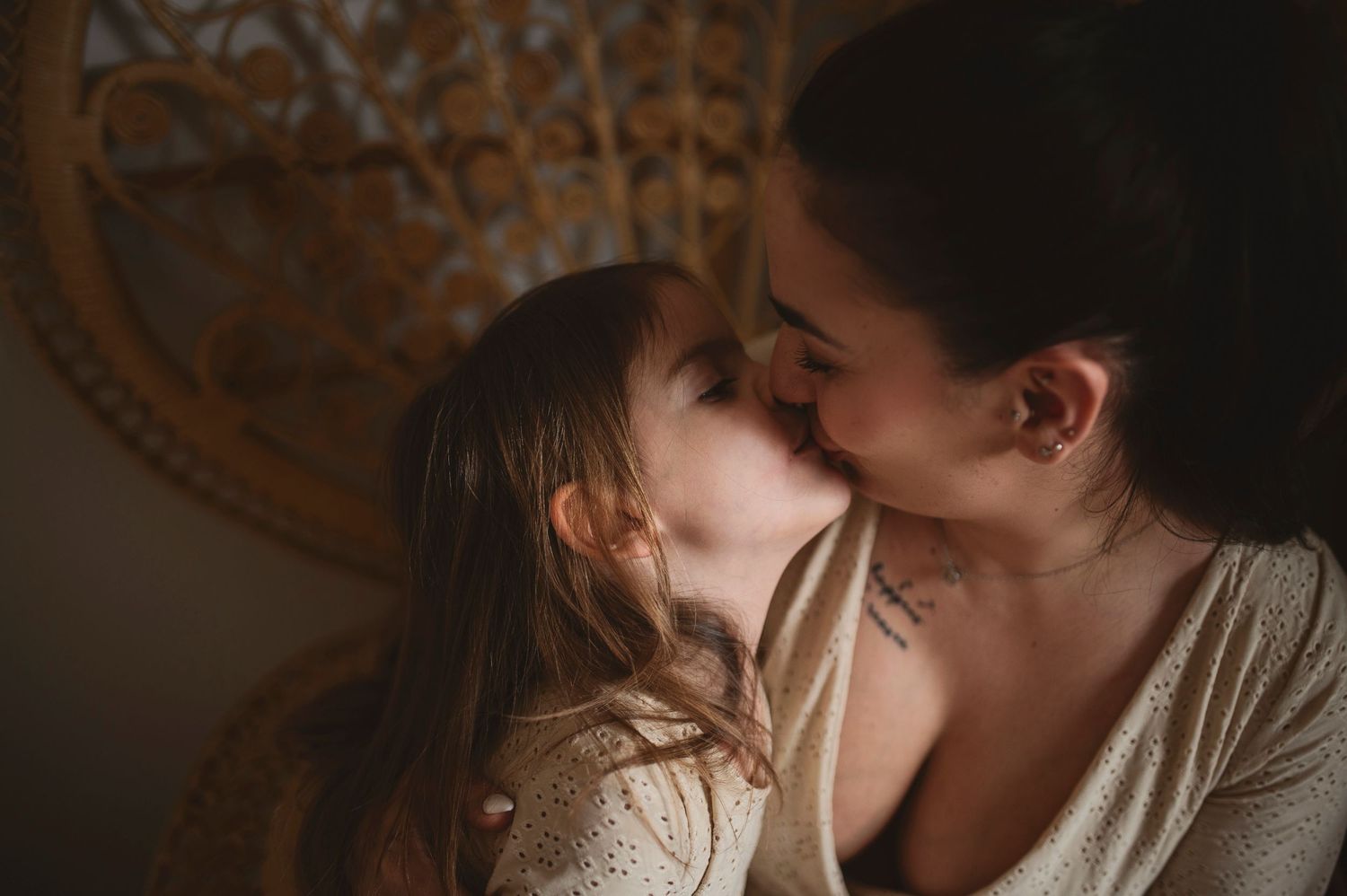 Intimate portrait of shared tender moment on a woven peacock chair with warm lighting.