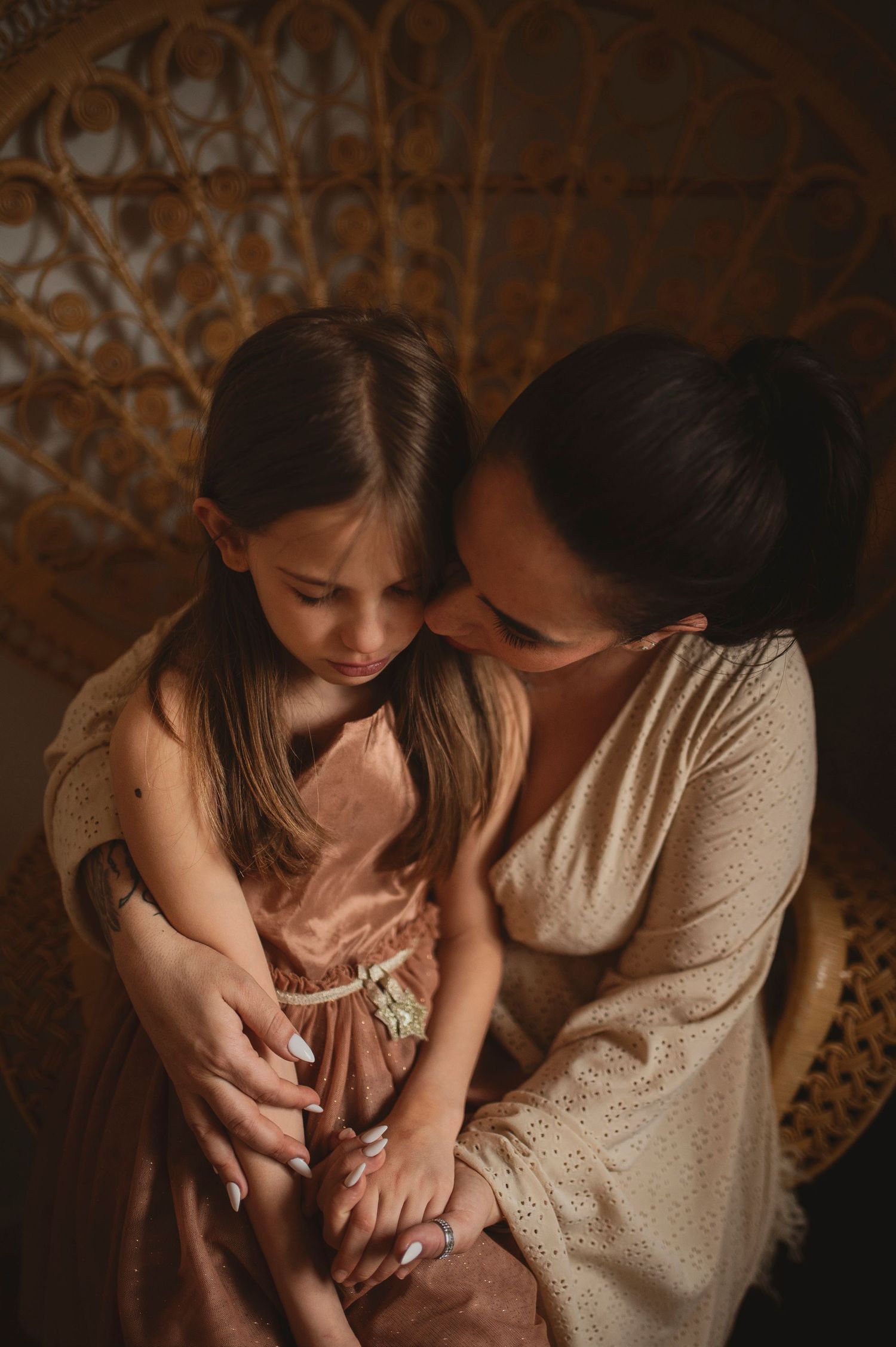 Tender embrace captured in warm tones against an ornate wicker chair backdrop.
