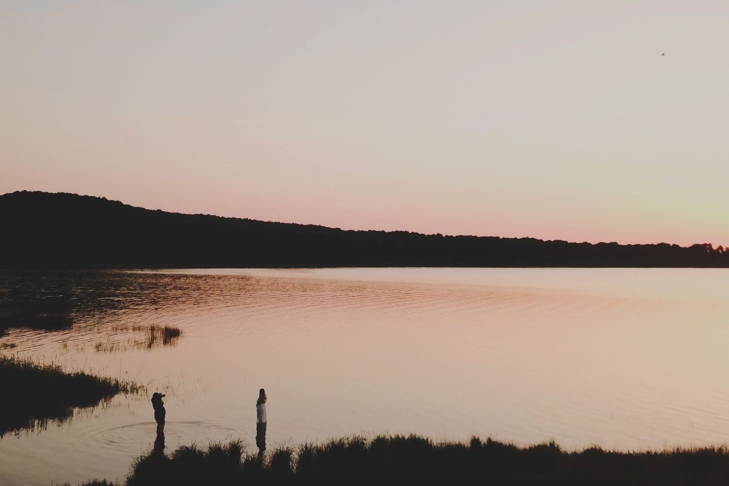 Drönarbild av gravidfotografering i Skåne där en gravid kvinna står i vattnet vid solnedgången.