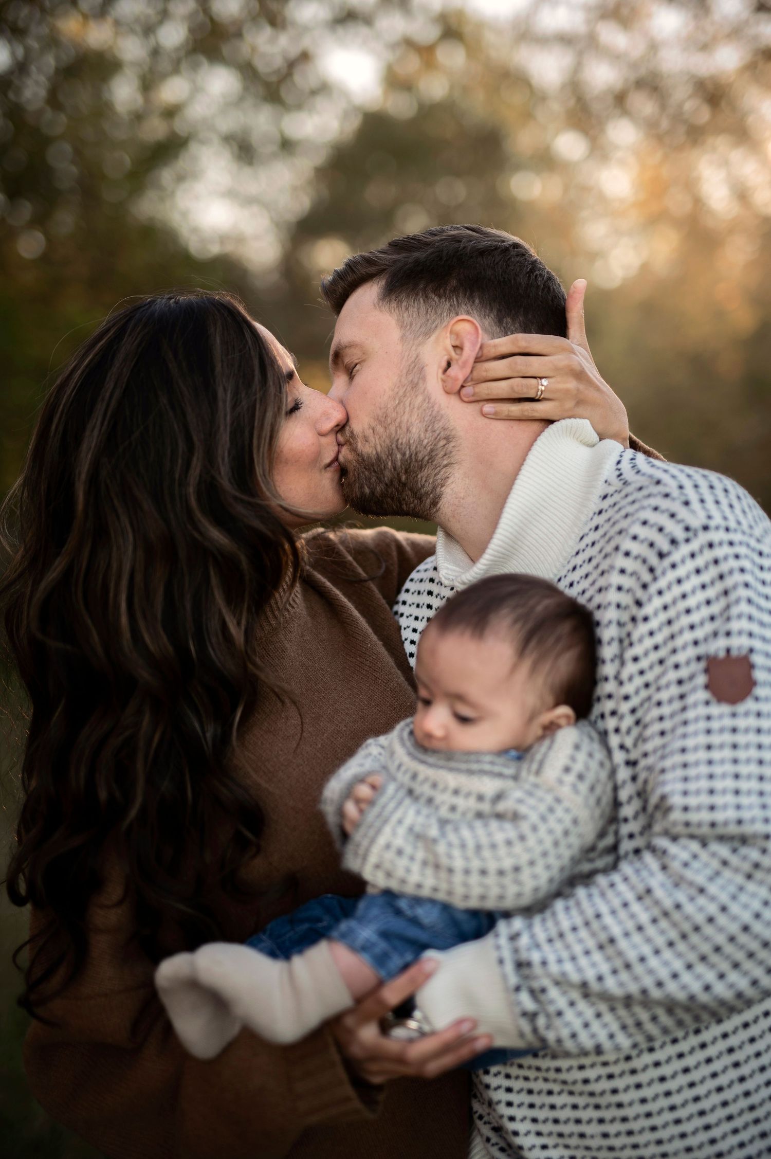 Familjefotografering i Skåne med föräldrar som kysser varandra och håller nyfödd i höstmiljö.