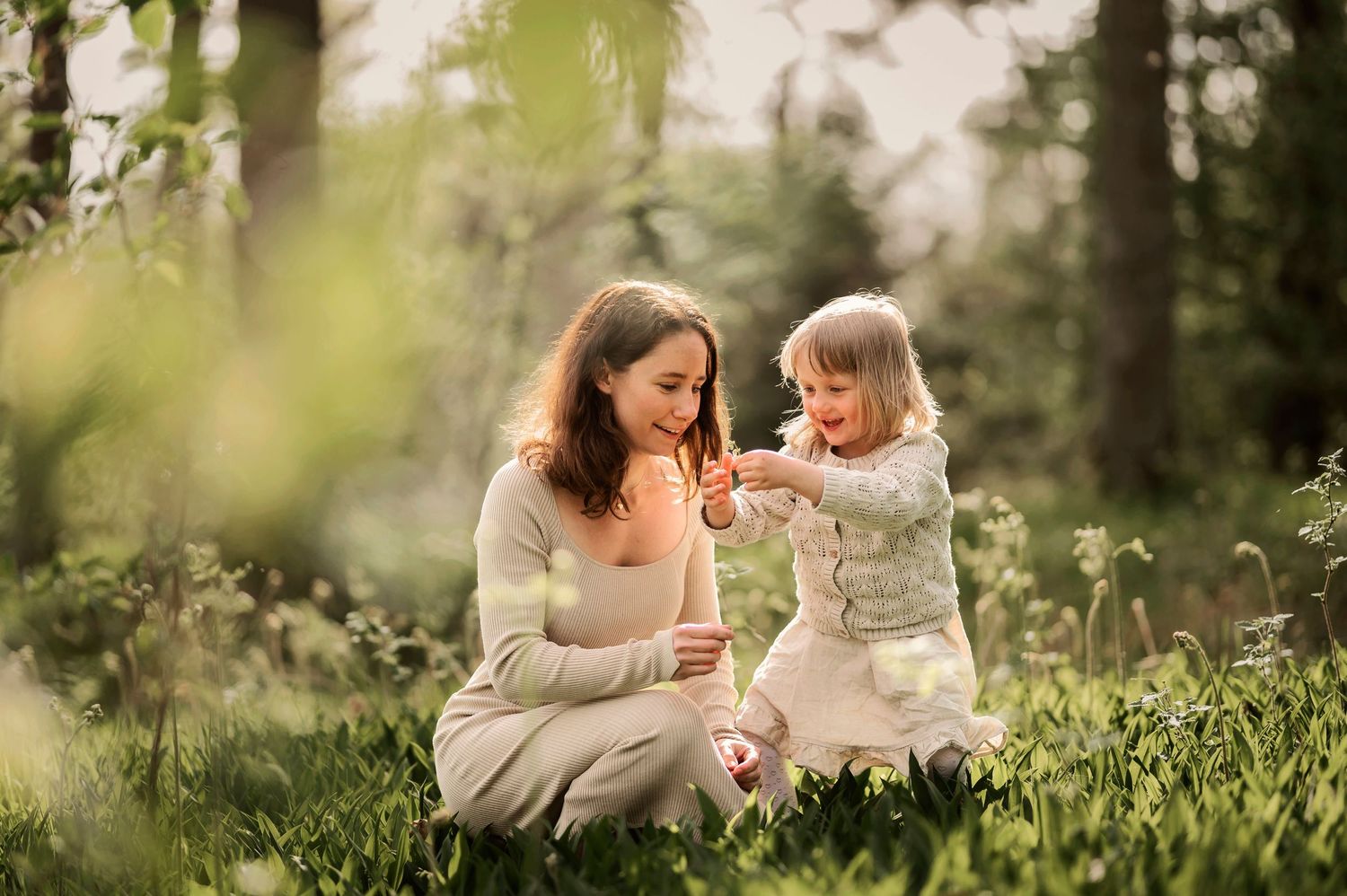 Familjefotografering i Skåne med mamma och småbarn i lekfullt ögonblick i solbelyst grön äng.