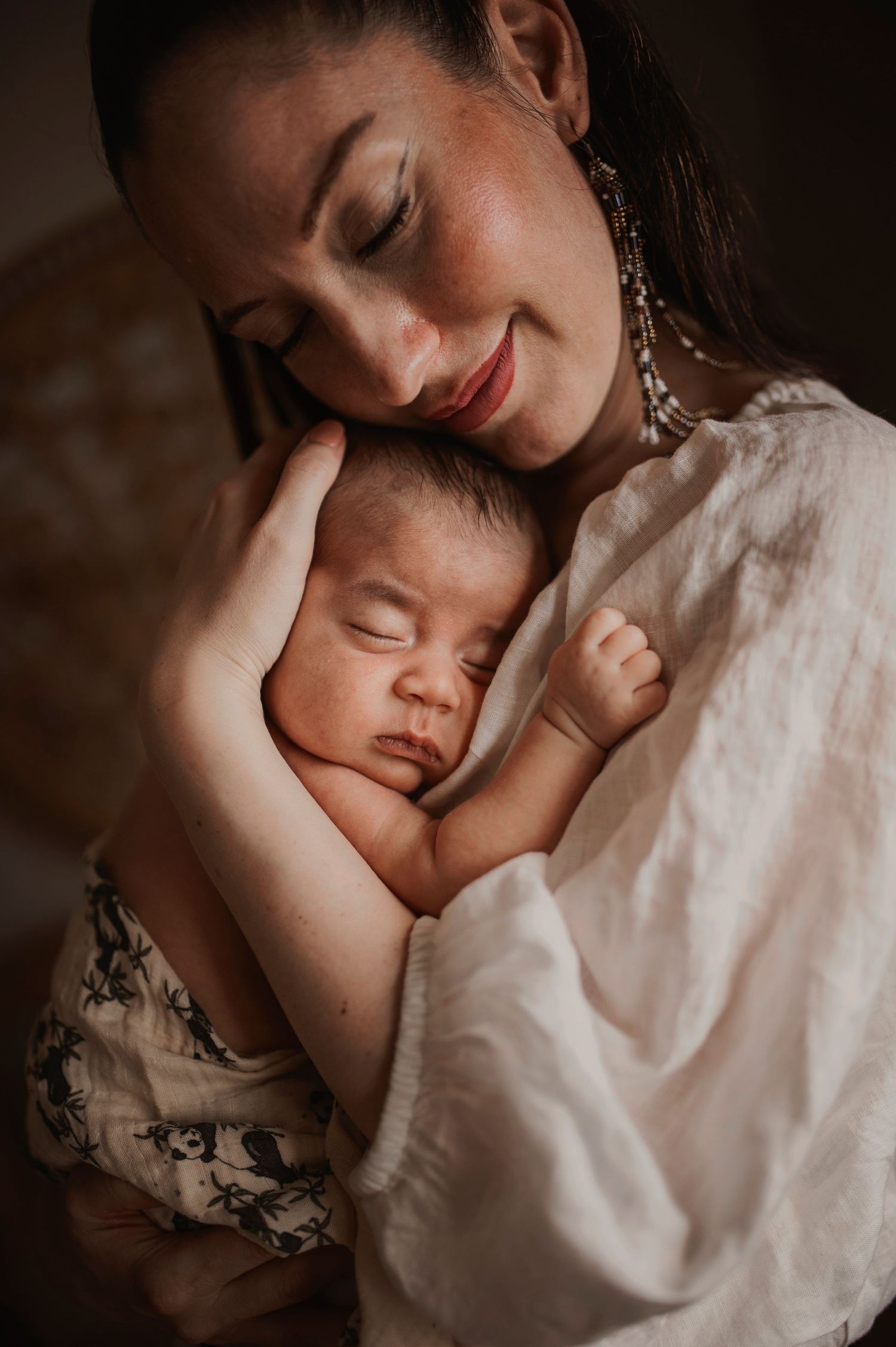 Intimate portrait of caregiver cradling sleeping infant against white lace dress.