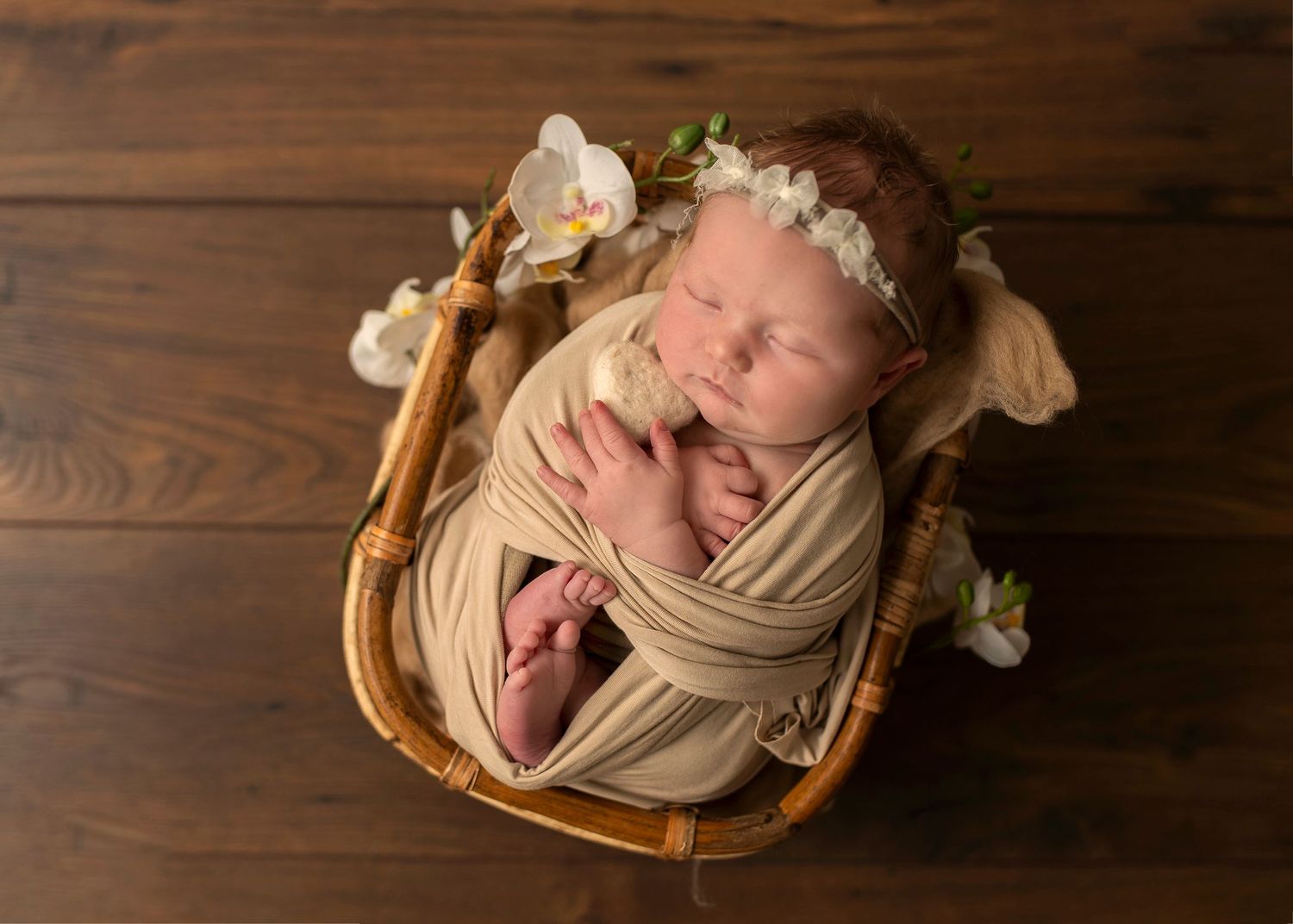 Nyföddfotografering i Skåne med sovande bebis på beige tyg i studio på träyta.
