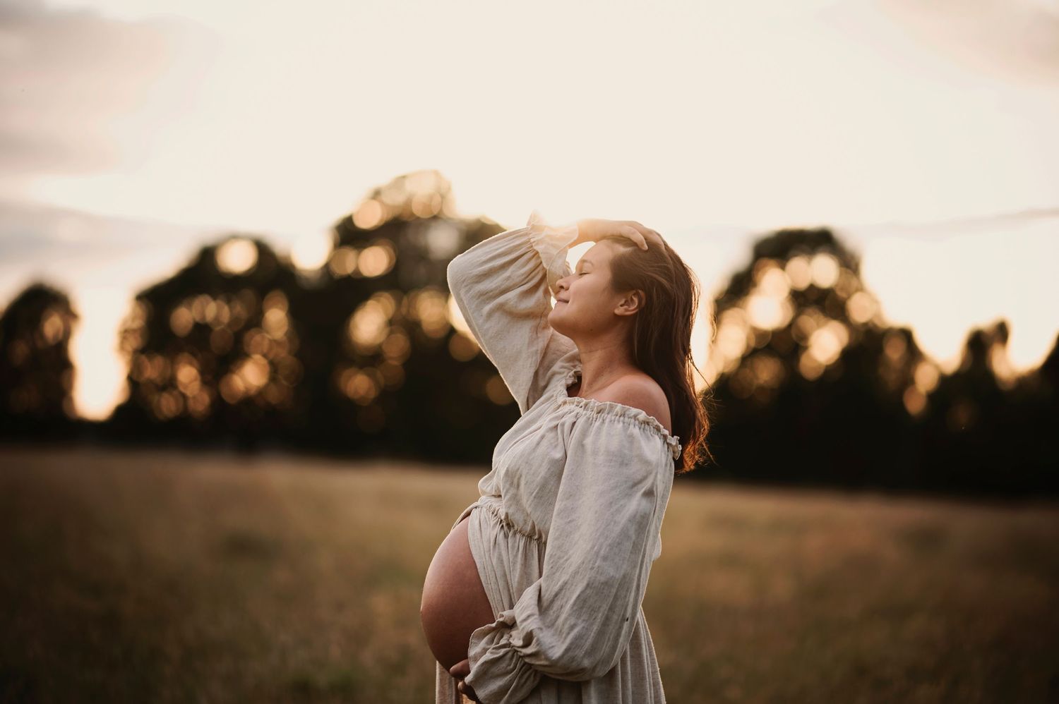 A joyful sunset maternity portrait in a rustic field with dramatic lighting.