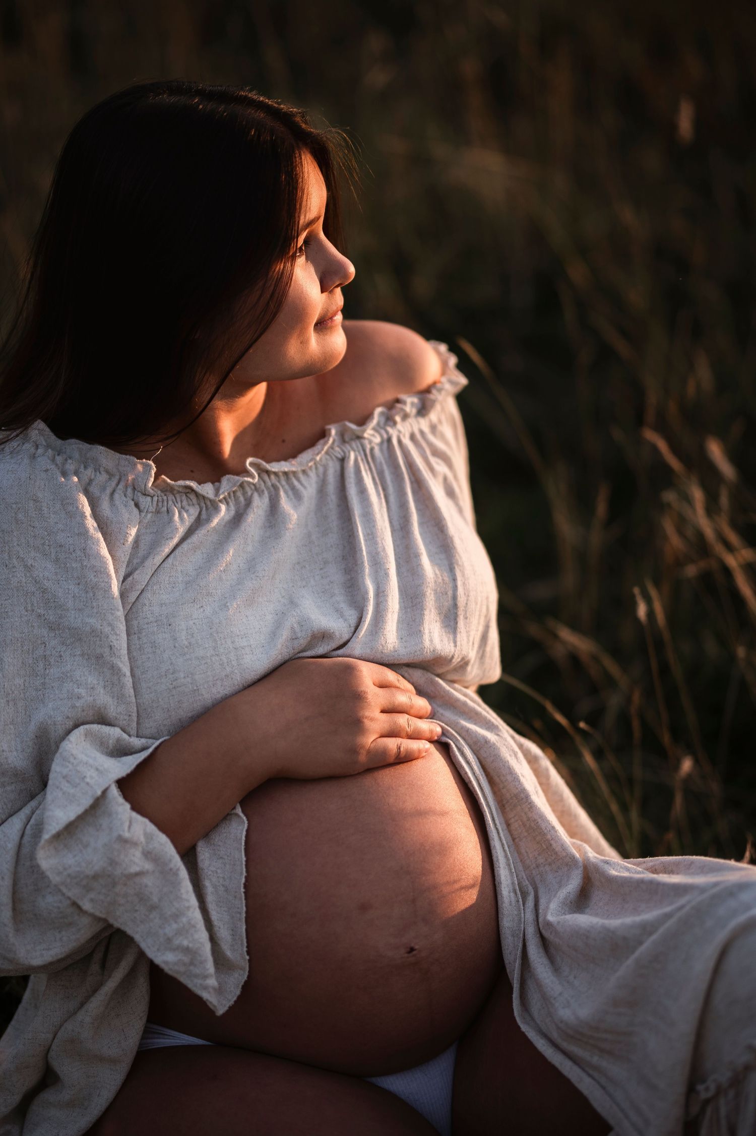 Maternity portrait showing silhouette against warm sunset light in field.