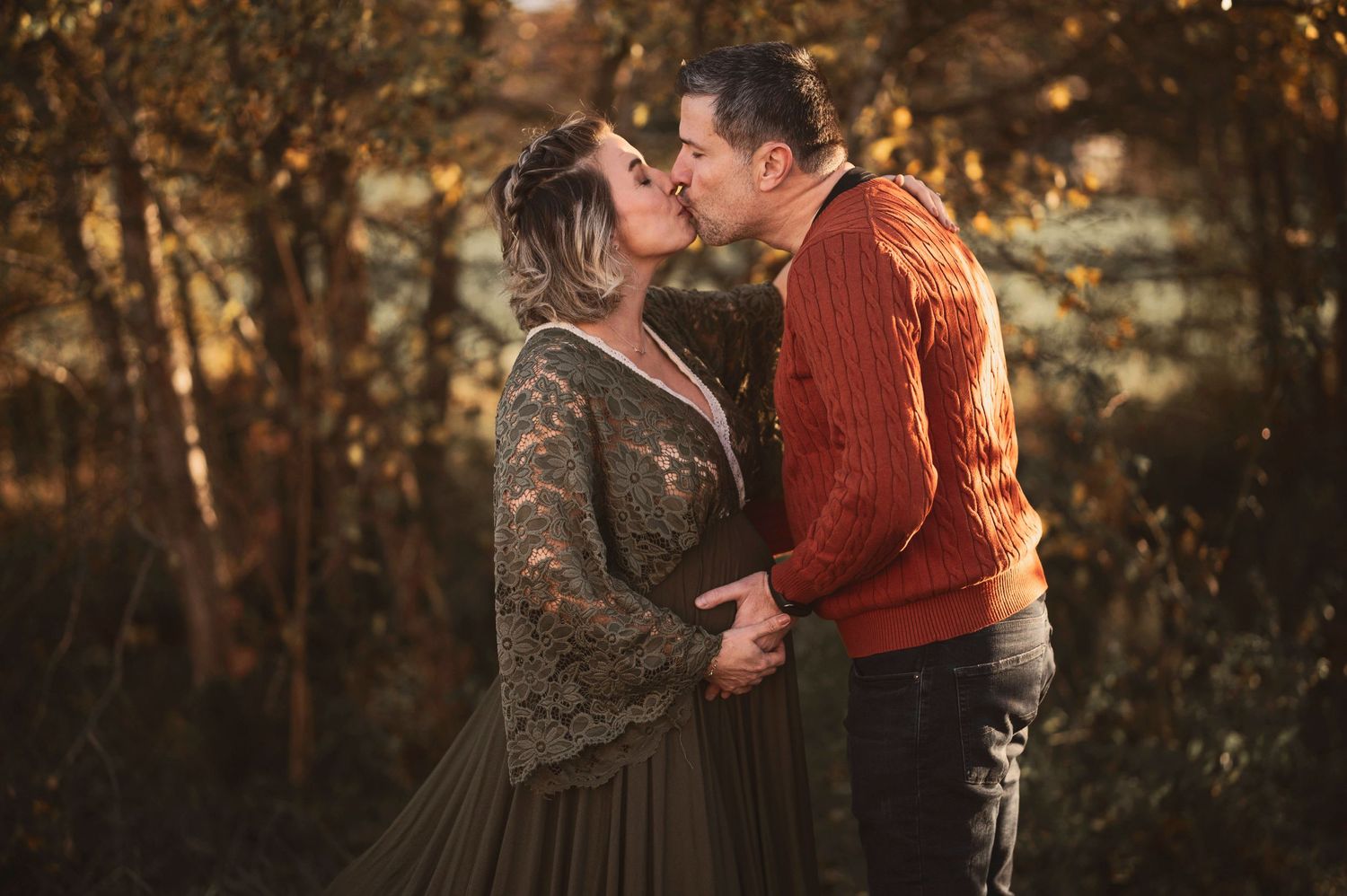 A romantic autumn sunset portrait shows a couple sharing an intimate kiss in a forest setting.