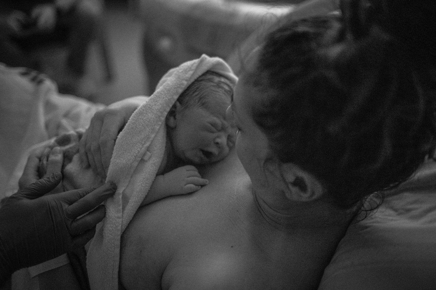 Svartvit nyföddfotografering i Skåne med mamma som håller sin nyfödda bebis nära bröstet efter förlossningen.
