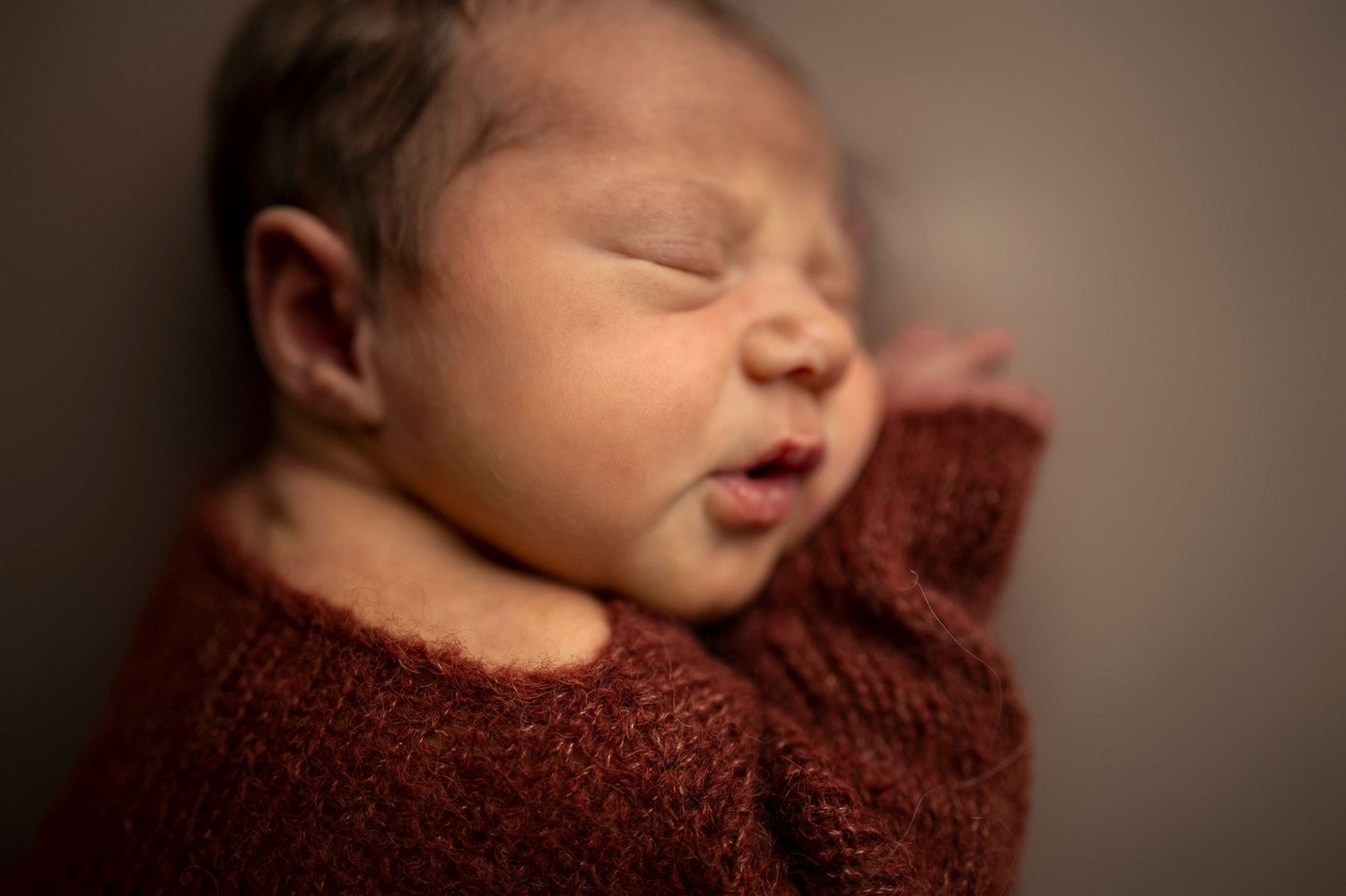 Nyföddfotografering i Hässleholm med en sovande bebis i mörkröd onesie i studio.